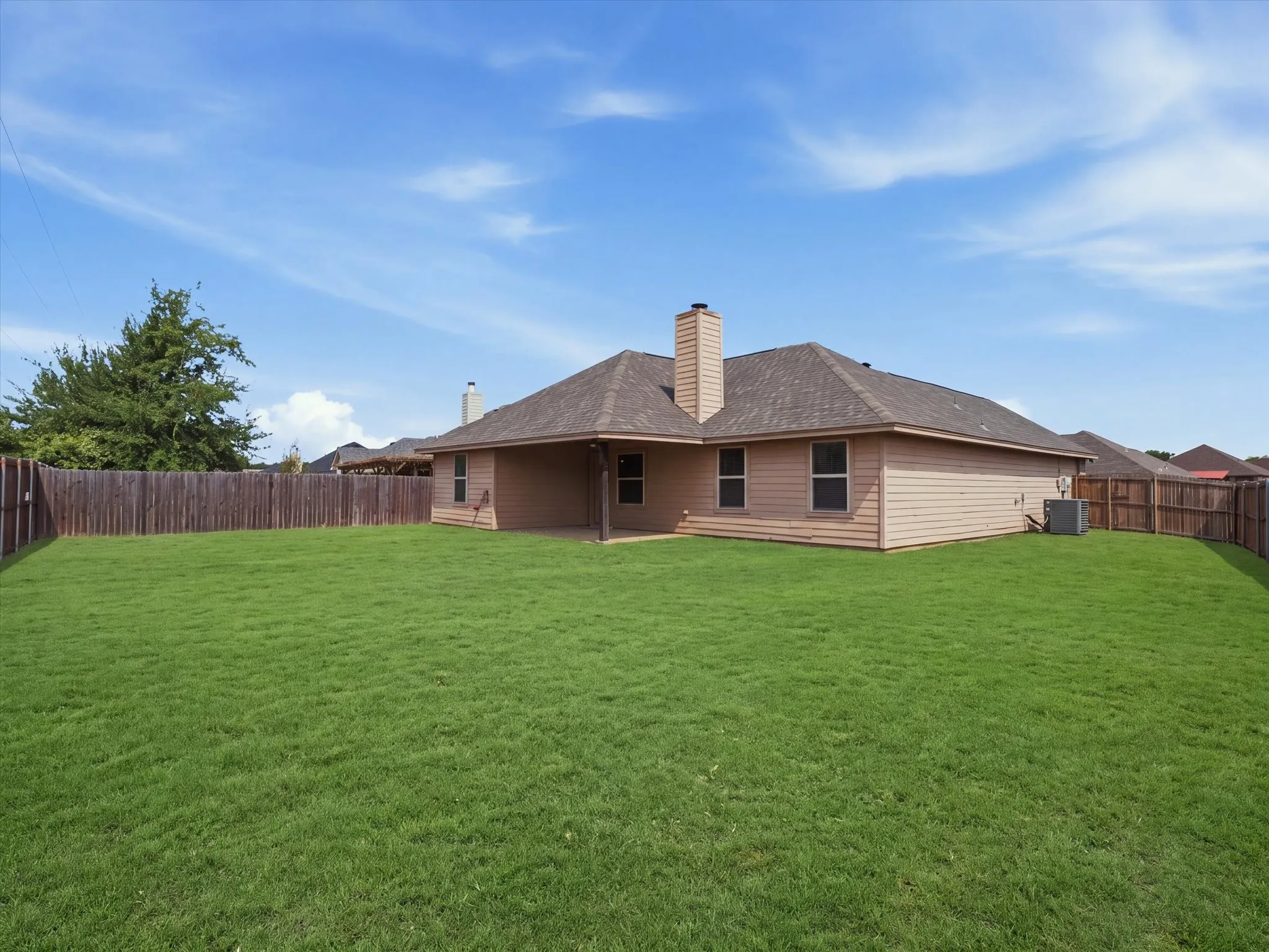 Expansive backyard featuring a manicured lawn, full privacy fencing, and a covered patio area