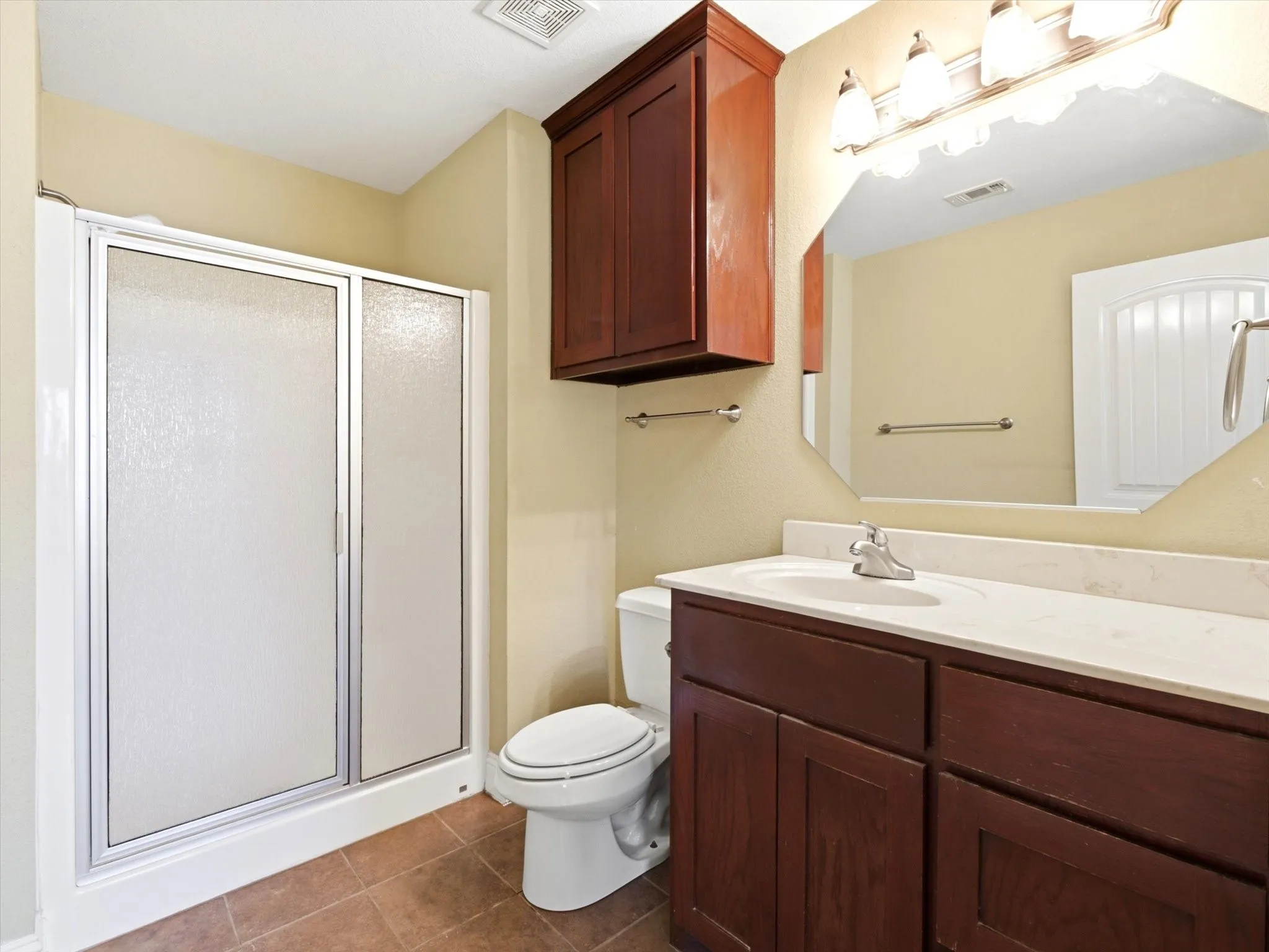 Spa-inspired master bathroom showcasing rich wood cabinetry with ample storage, a spacious countertop with integrated sink and chrome fixtures, a large framed mirror with integrated lighting, and a separate enclosed shower with sliding glass doors