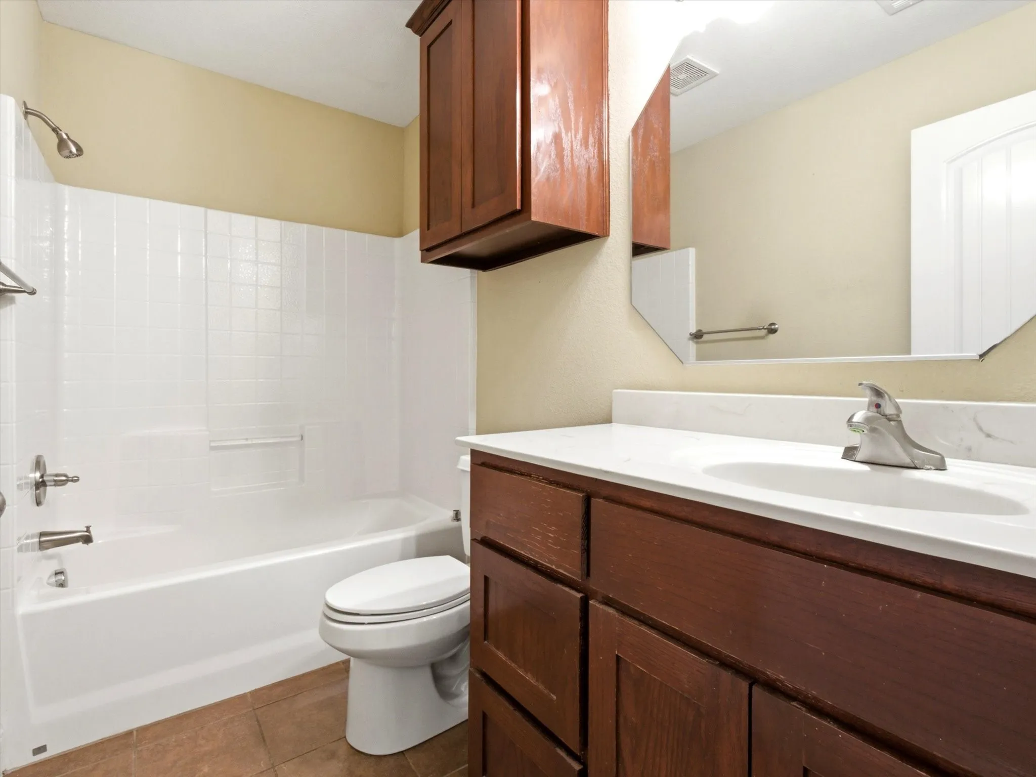 Bathroom featuring a white tub/shower combination with chrome fixtures, a toilet, and warm-toned floor tiles