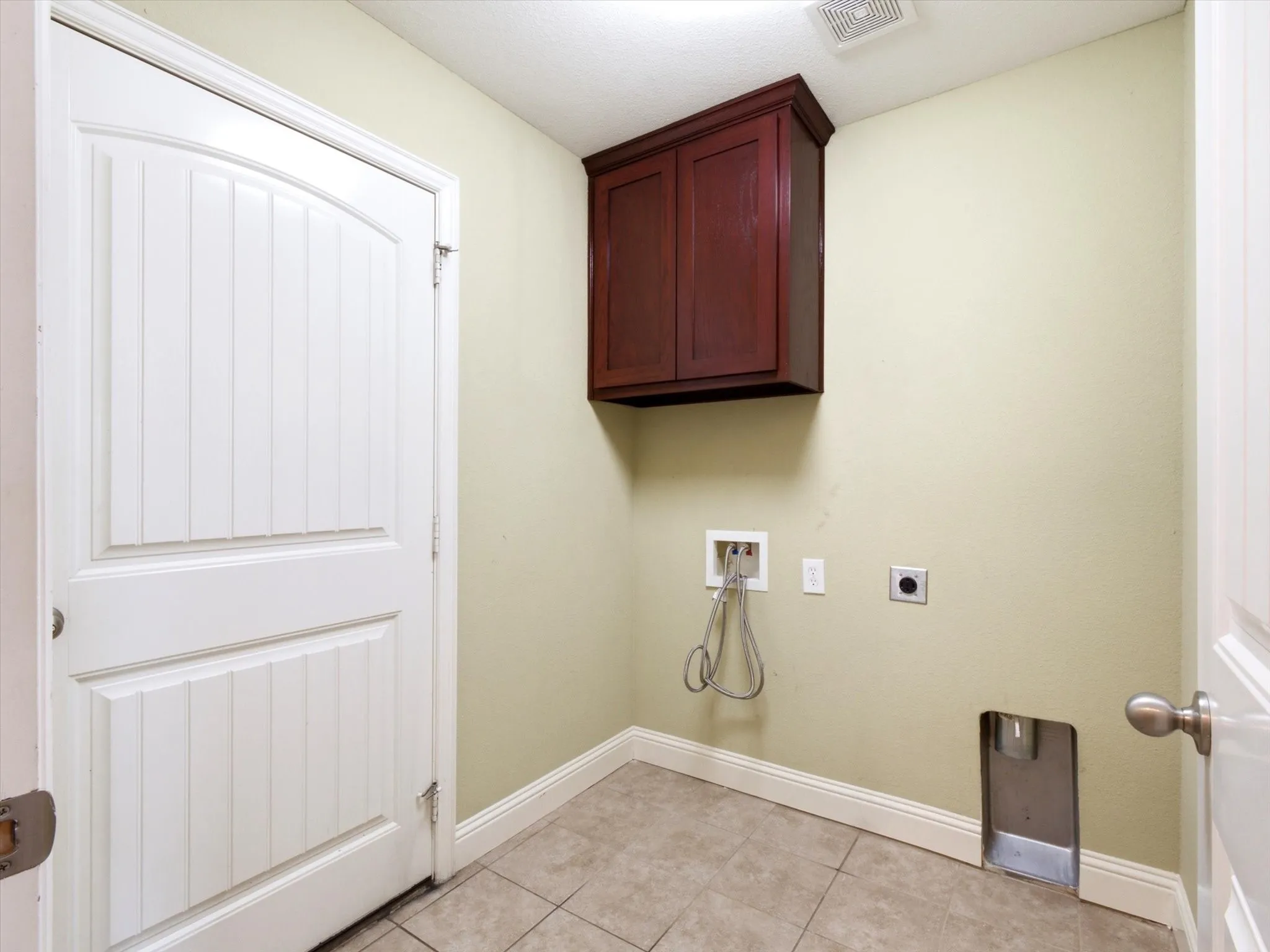 Utility area featuring light neutral wall paint, tiled flooring, white baseboards, and a dark wood-finish wall cabinet