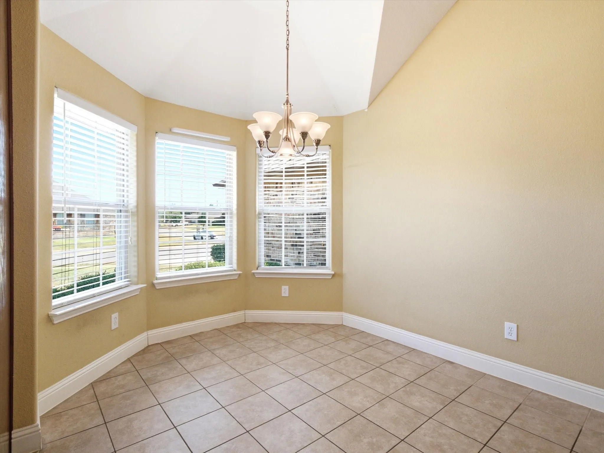 Bright sunroom featuring expansive bay windows with plantation shutters, neutral wall finishes, ceramic tile flooring, crown molding, and a suspended multi-light fixture that floods the space with natural light