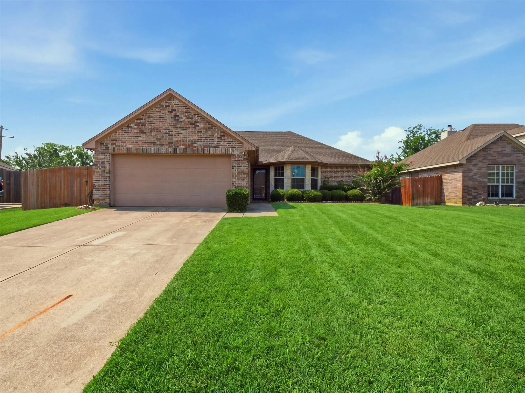 Brick exterior home featuring a two-car garage, concrete driveway, and a fenced side yard