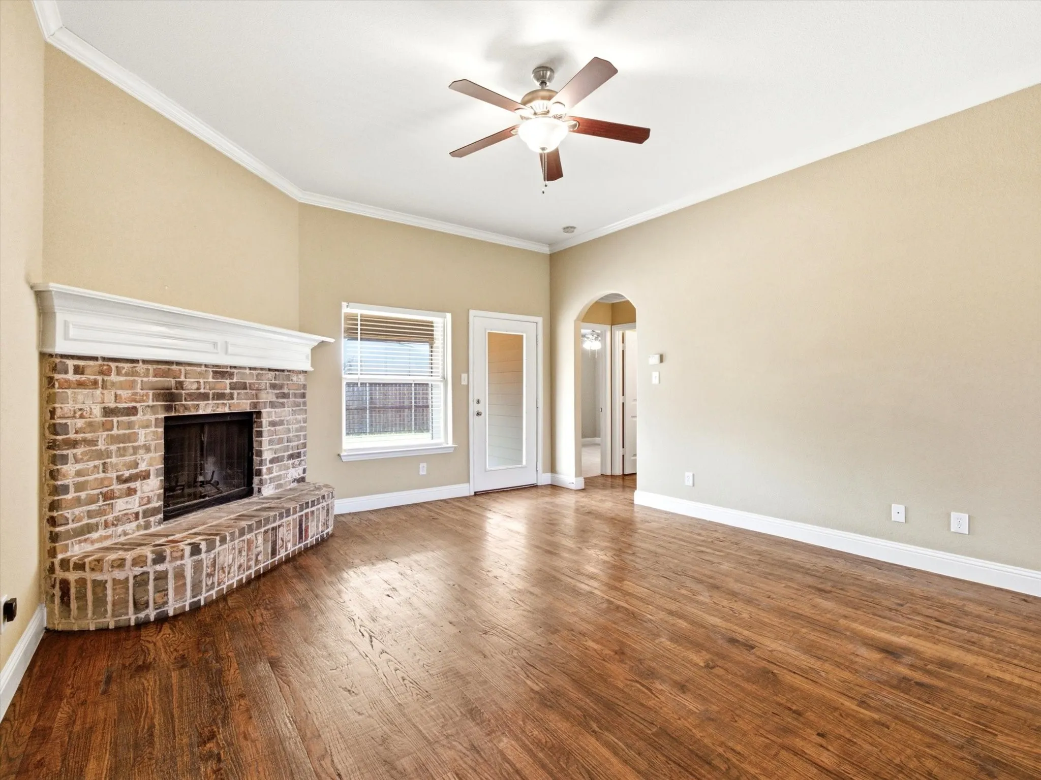 Brick fireplace with a white mantel, wood-finish flooring, and a ceiling fan