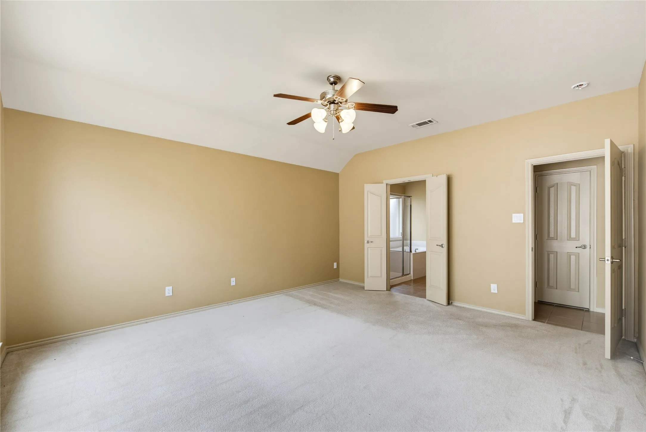 Spacious downstairs primary bedroom with vaulted ceilings and a ceiling fan.
