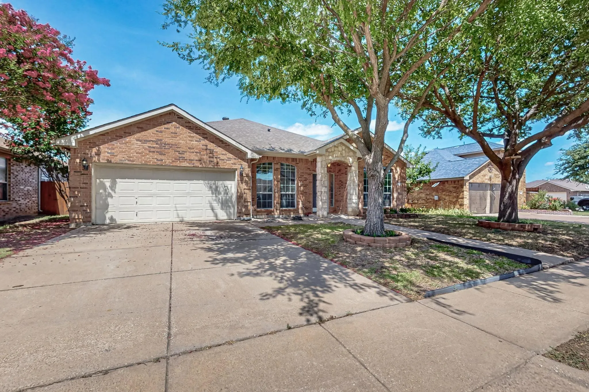 Single story home with brick siding, an attached garage, driveway, and a shingled roof