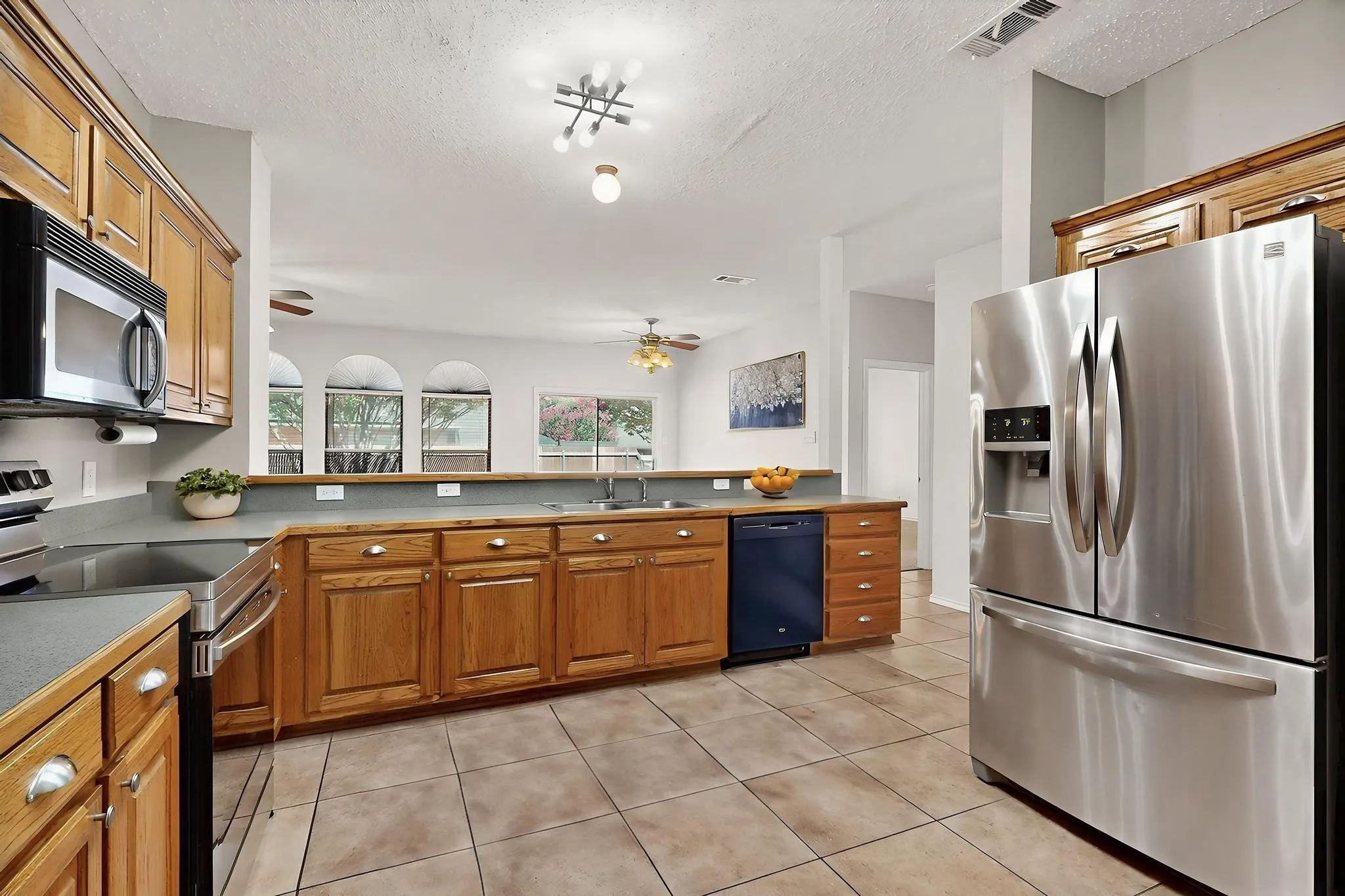 Kitchen featuring appliances with stainless steel finishes, brown cabinetry, a textured ceiling, a ceiling fan, and light tile patterned floors  *Virtually staged
