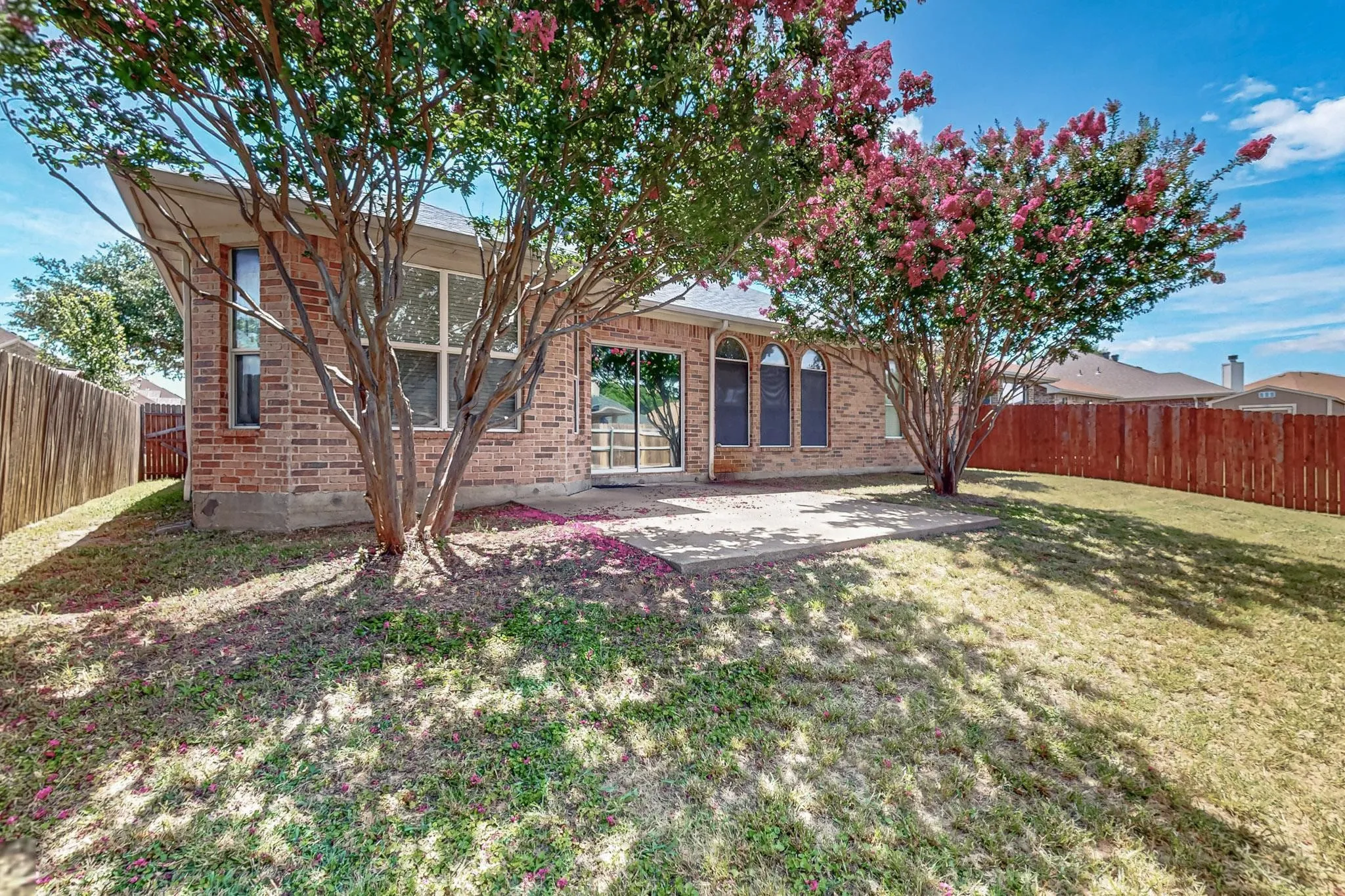 Rear view of property with brick siding, a fenced backyard, and a patio area