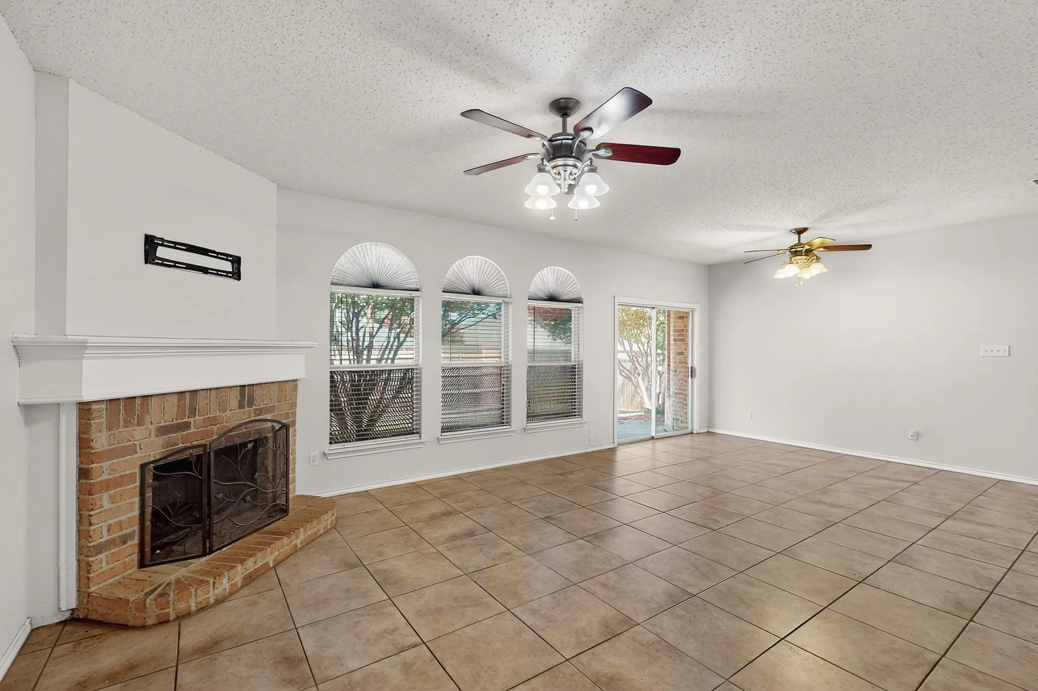 Unfurnished living room featuring light tile patterned floors, a textured ceiling, ceiling fan, and a fireplace
