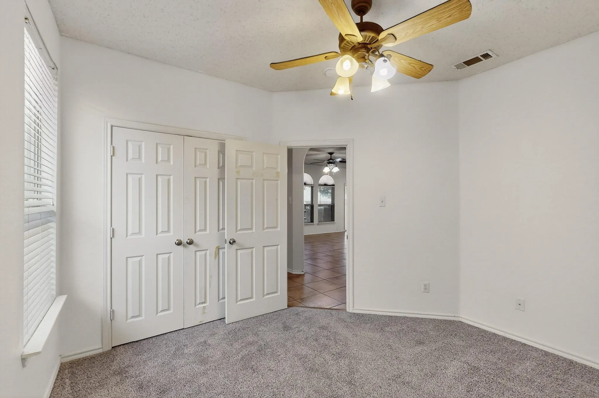 Unfurnished bedroom with carpet floors, a closet, tile patterned floors, and a ceiling fan