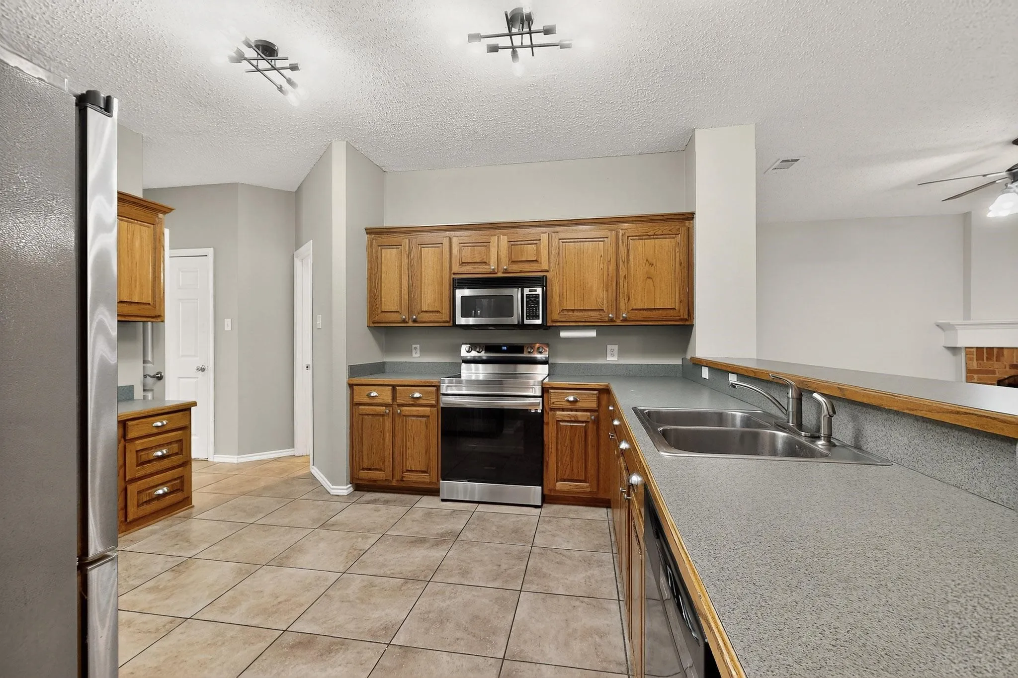 Kitchen featuring stainless steel appliances, light tile patterned floors, a ceiling fan, brown cabinets, and a textured ceiling