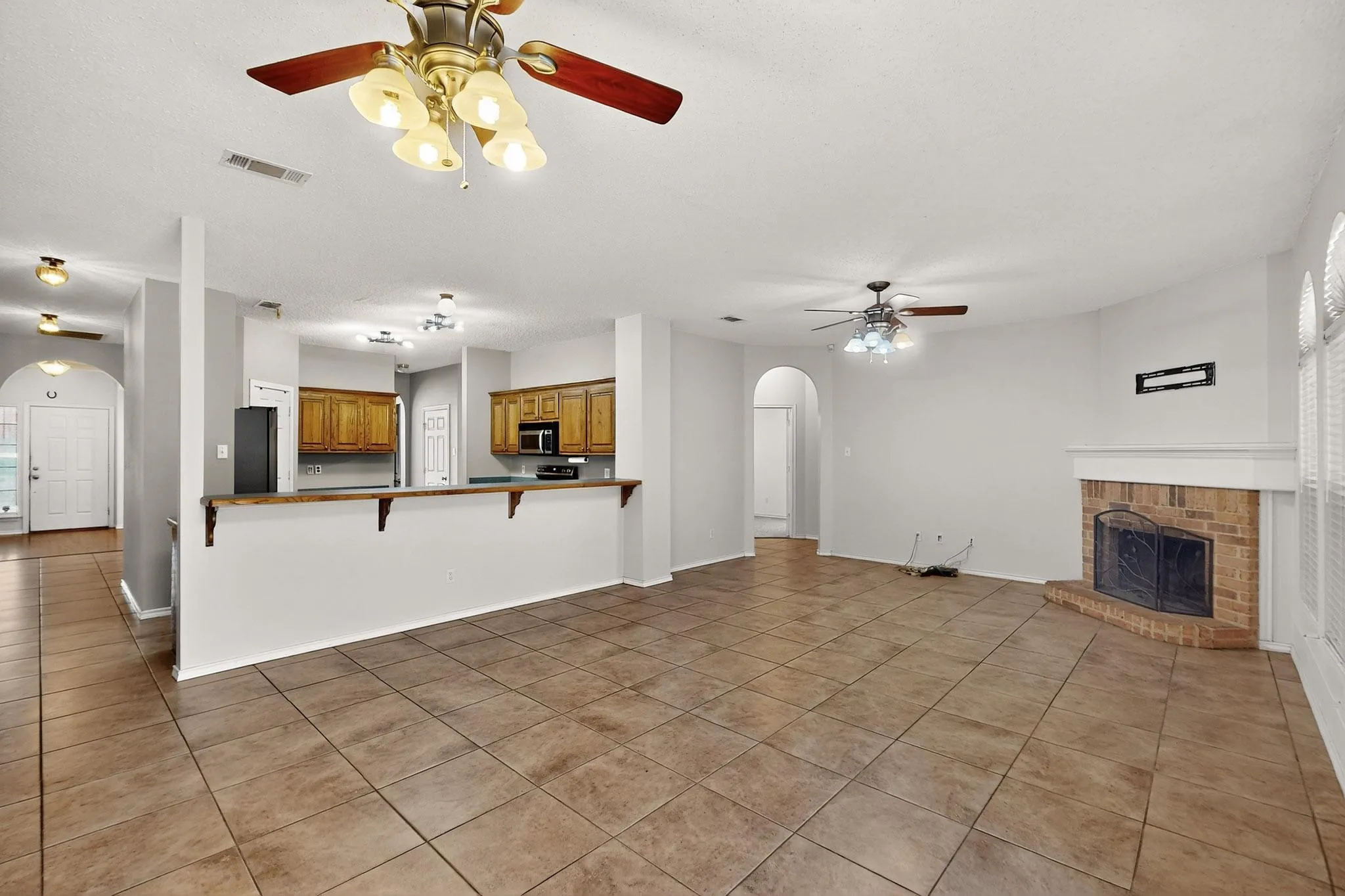Unfurnished living room featuring a ceiling fan, arched walkways, light tile patterned floors, and a brick fireplace