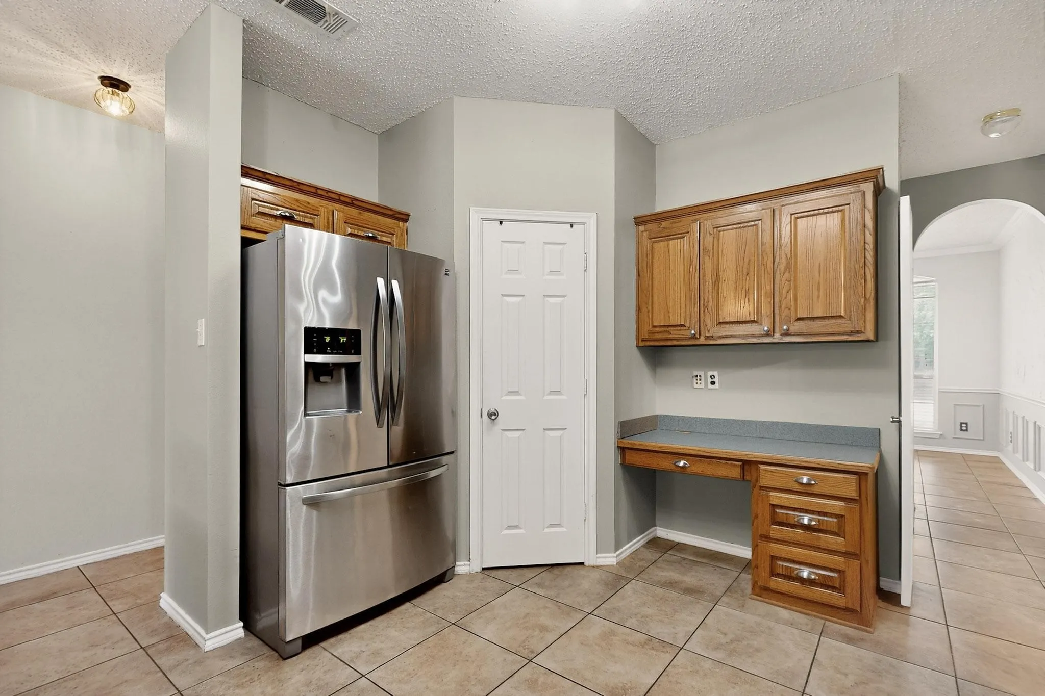 Kitchen with stainless steel refrigerator with ice dispenser, built in desk, arched walkways, light tile patterned floors, and a textured ceiling