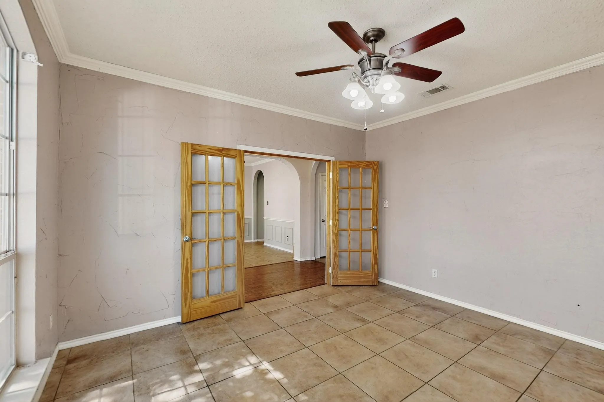 Unfurnished room featuring arched walkways, crown molding, a ceiling fan, light tile patterned floors, and a textured ceiling