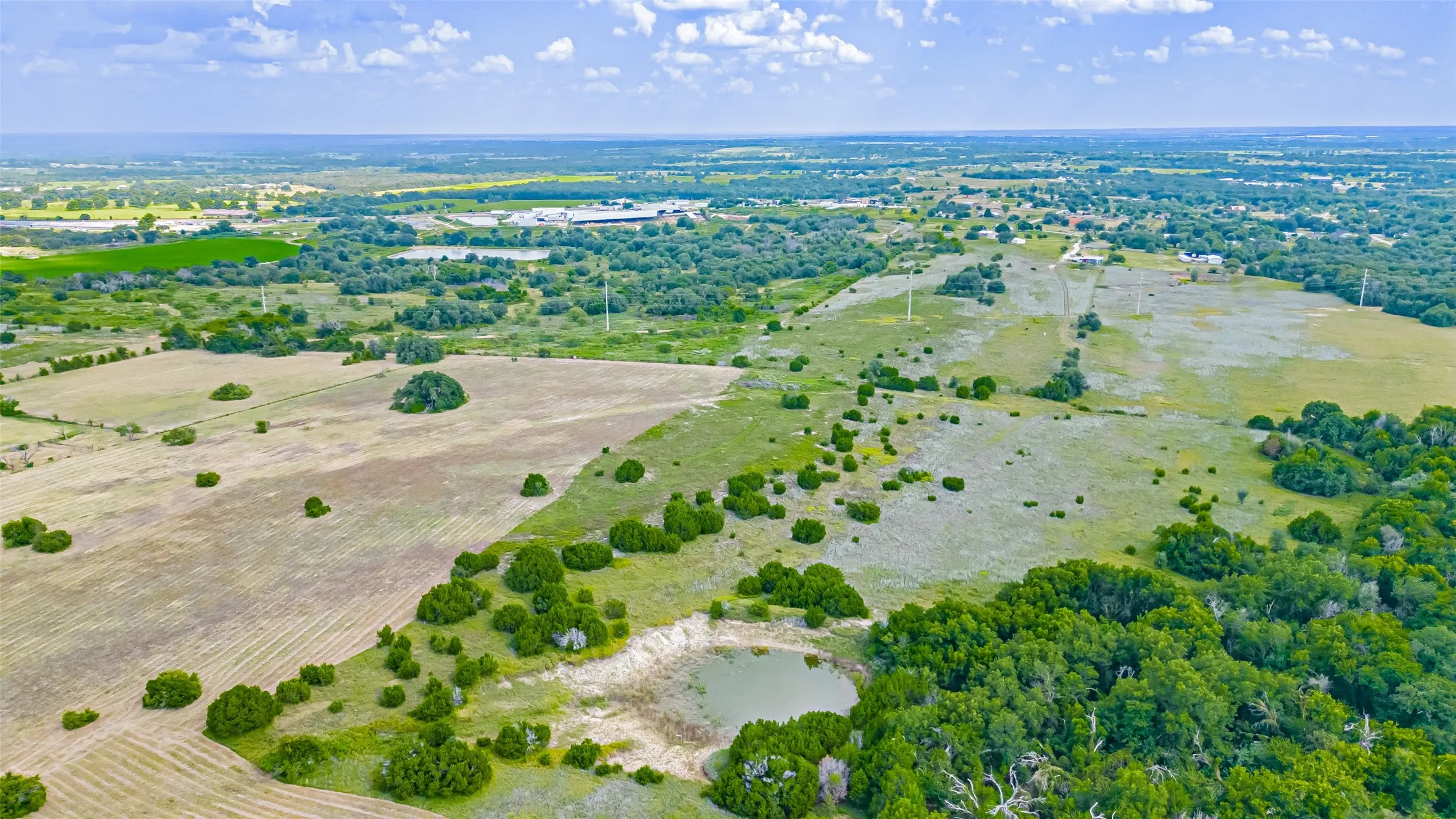 Expansive rural landscape featuring a mix of cultivated fields, natural woodlands, and open grasslands