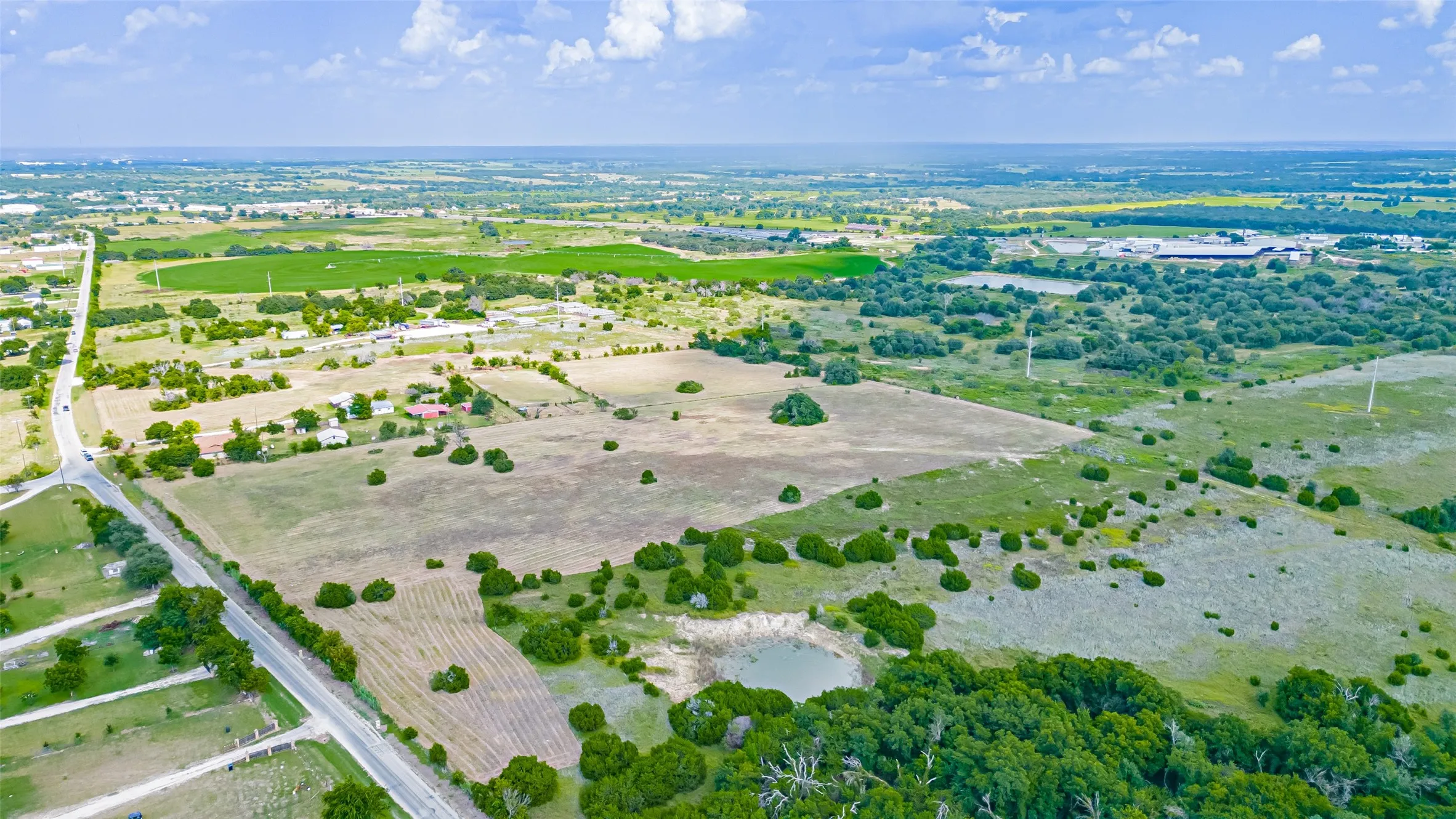 Expansive rural property featuring varied terrain, a visible roadway, and a natural water feature