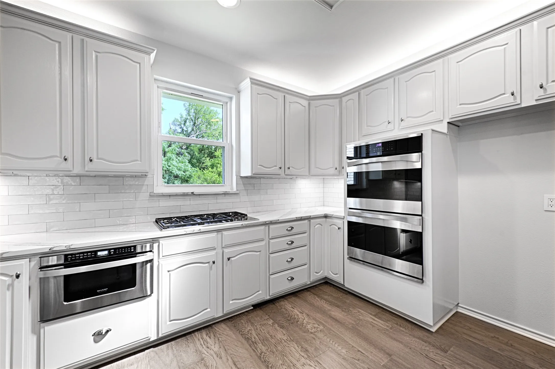 Kitchen featuring white cabinetry with crown molding, subway tile backsplash, light-toned countertops, a built-in WOLFE gas range, drawer microwave and double wall ovens