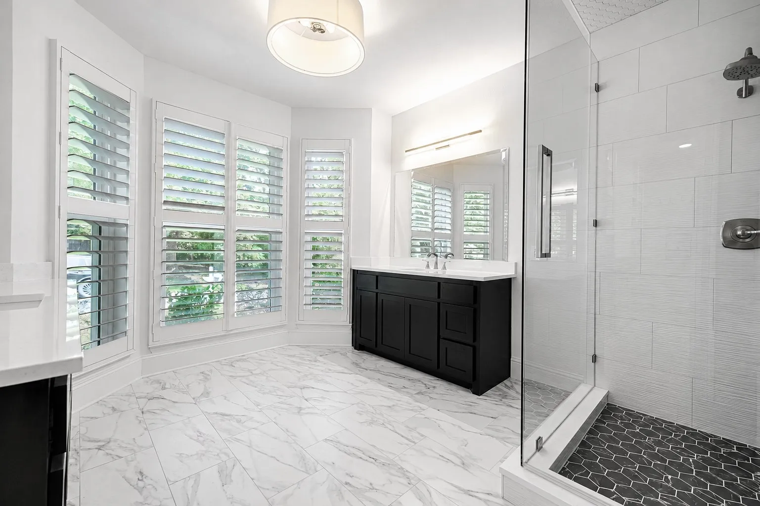 Spacious bathroom featuring a double vanity with black cabinetry and white countertops, a large frameless mirror, and marble-look tile flooring