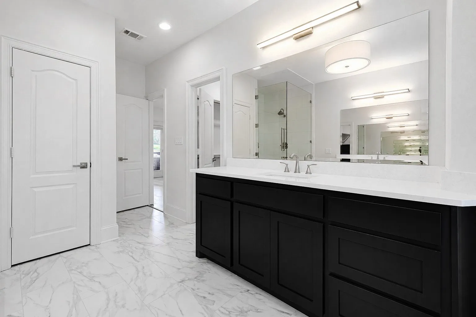 Spacious bathroom featuring a double vanity with black cabinetry and white countertops, a large frameless mirror, and marble-look tile flooring