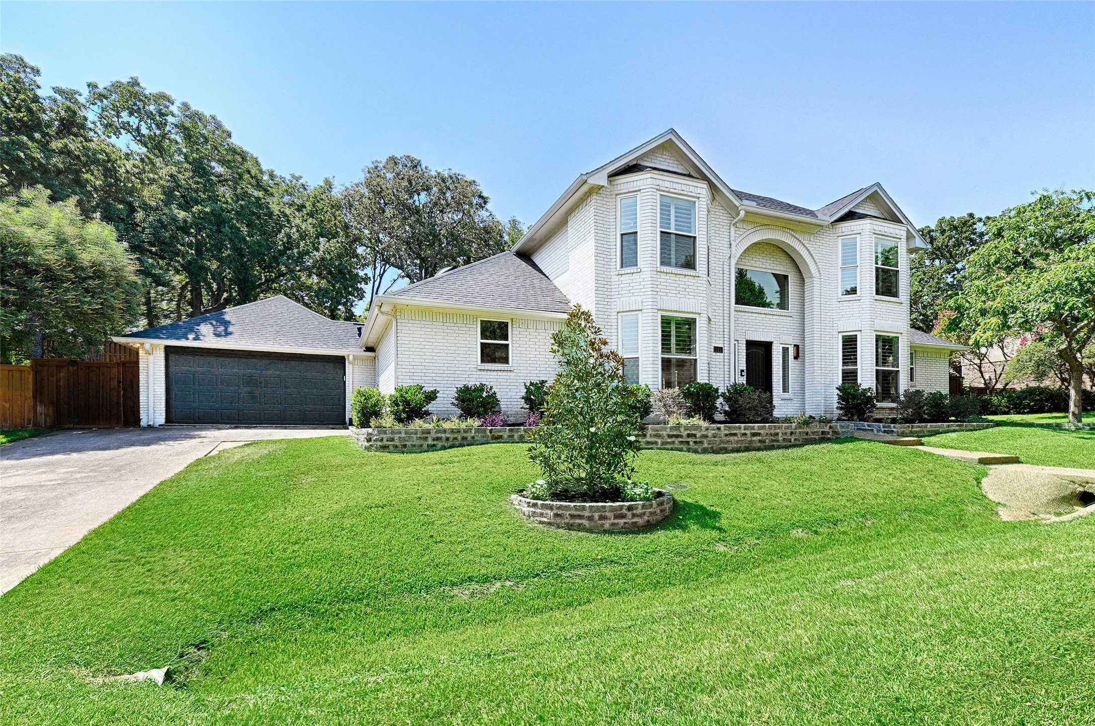 White brick residence featuring a prominent arched entry, multiple bay windows, and a multi-gabled roofline