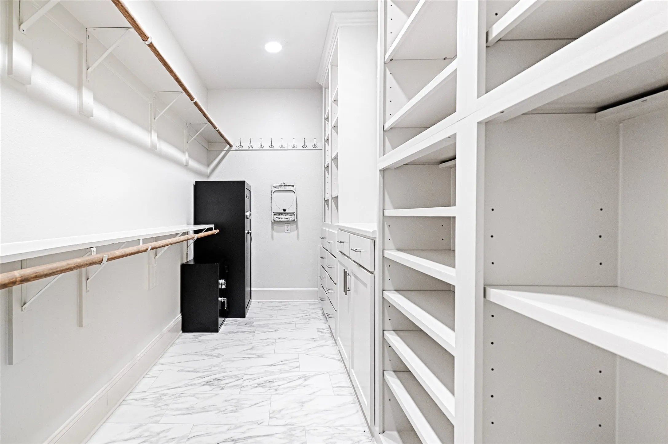 Walk-in closet featuring marble-look tile flooring, extensive built-in shelving, white cabinetry with drawers, and hanging rods