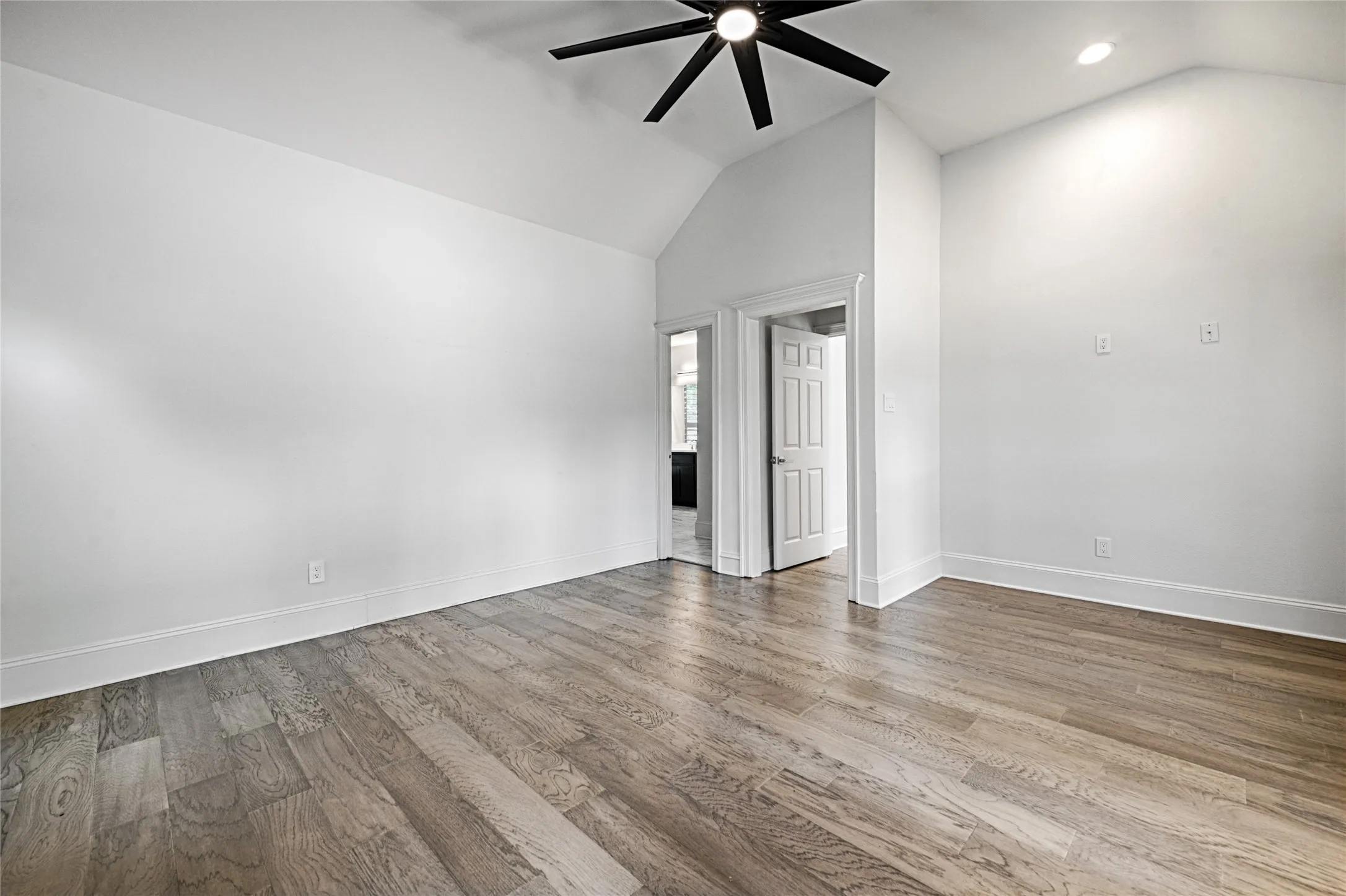 Vaulted ceiling bedroom with wood-finish flooring, featuring a ceiling fan and recessed lighting