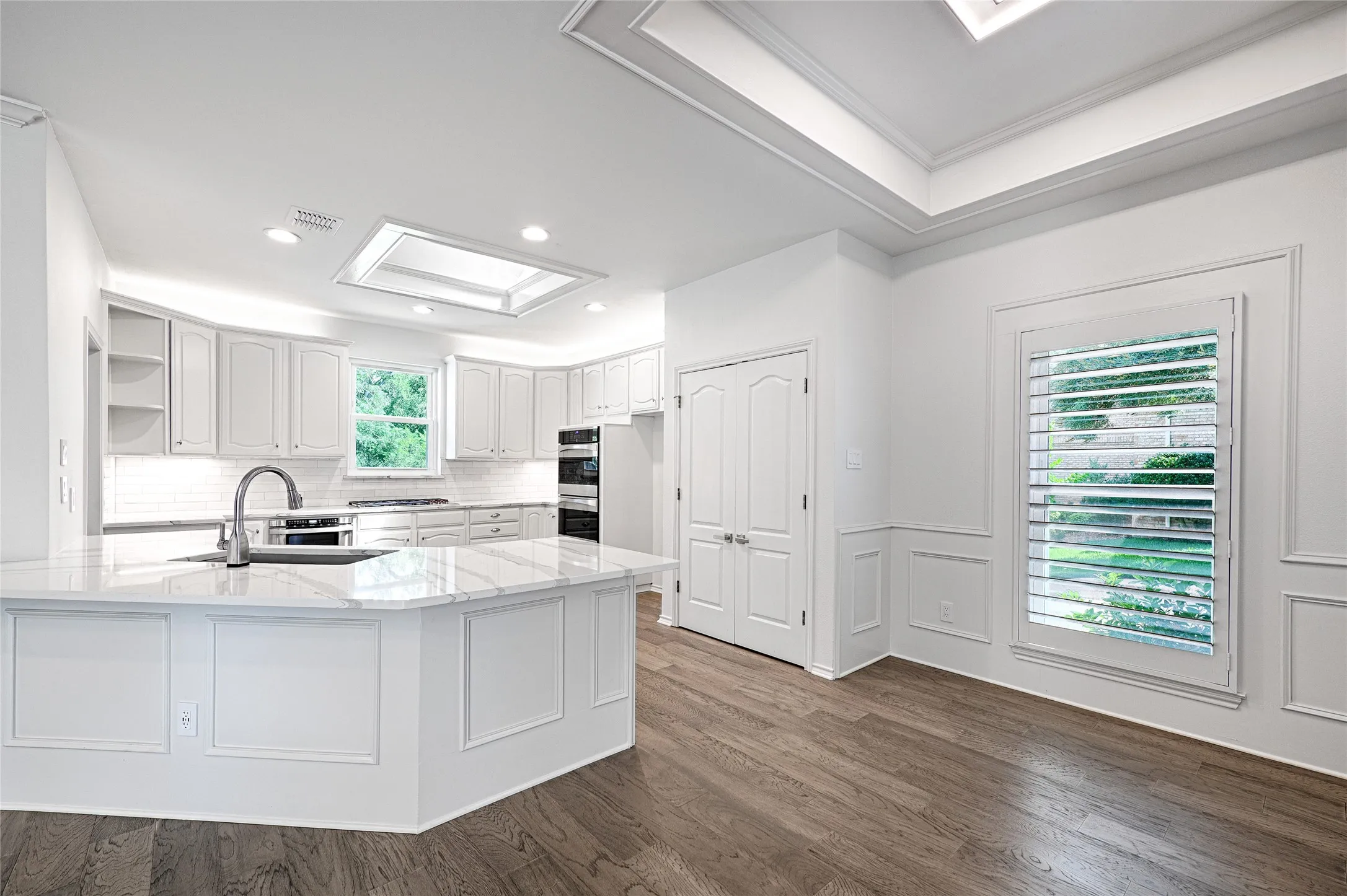 Spacious kitchen featuring skylight, white cabinetry, a large central island with a sink, white countertops, built-in double ovens, and recessed lighting