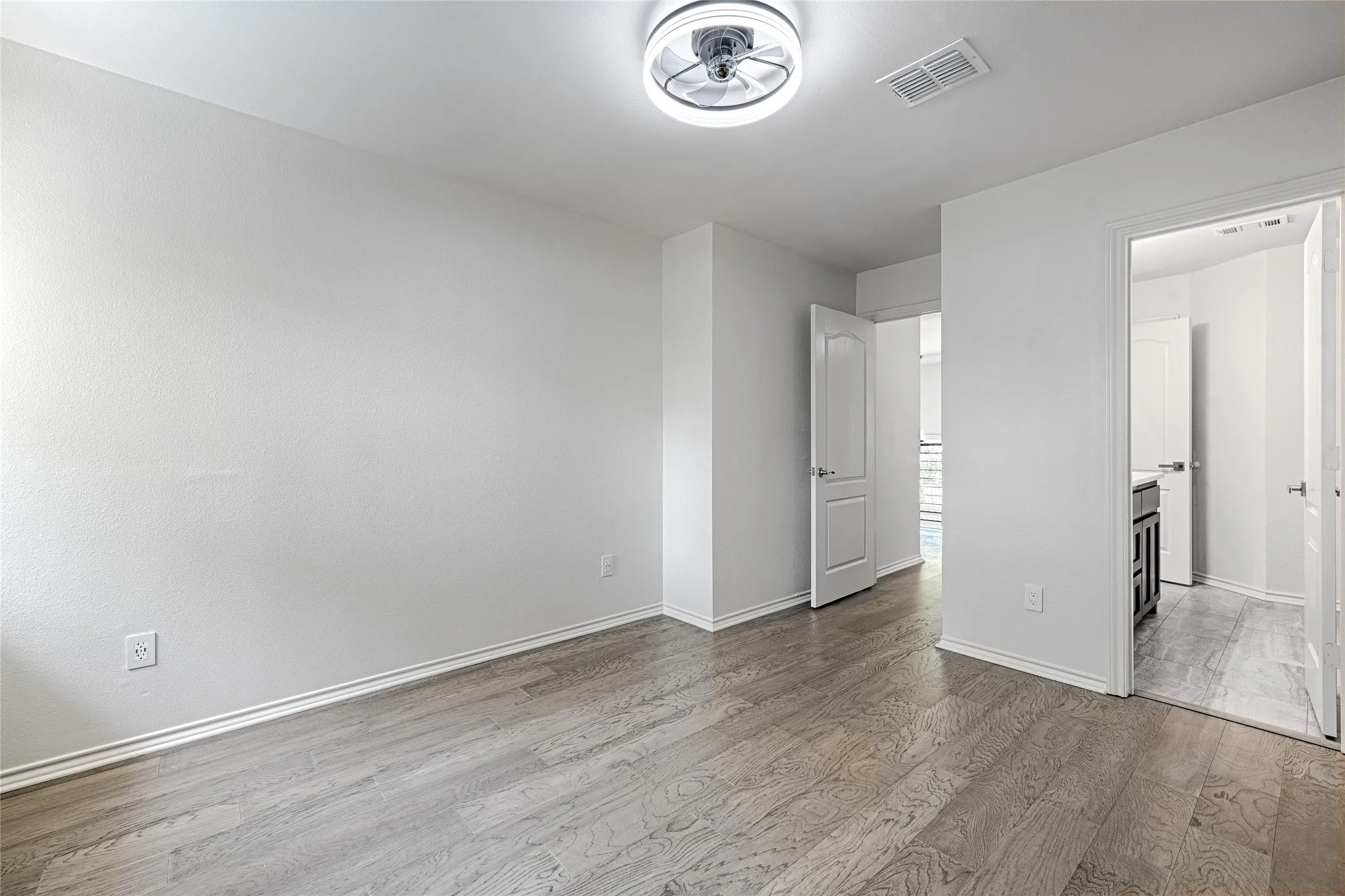 Secondary Bedroom with en-suite bath and walk-in closet, bay window with plantation shutters and wood-finish flooring. Bright interior space featuring wood-finish flooring, white baseboards, and a contemporary ceiling light fixture