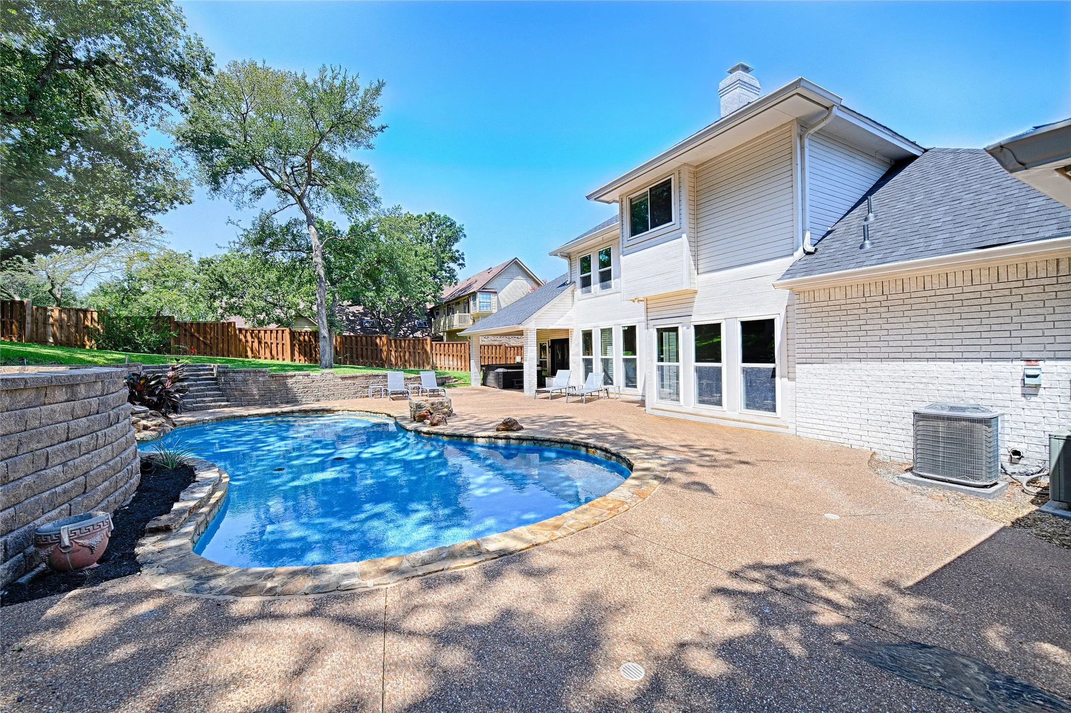 Curved swimming pool with stone coping surrounded by a textured concrete patio
