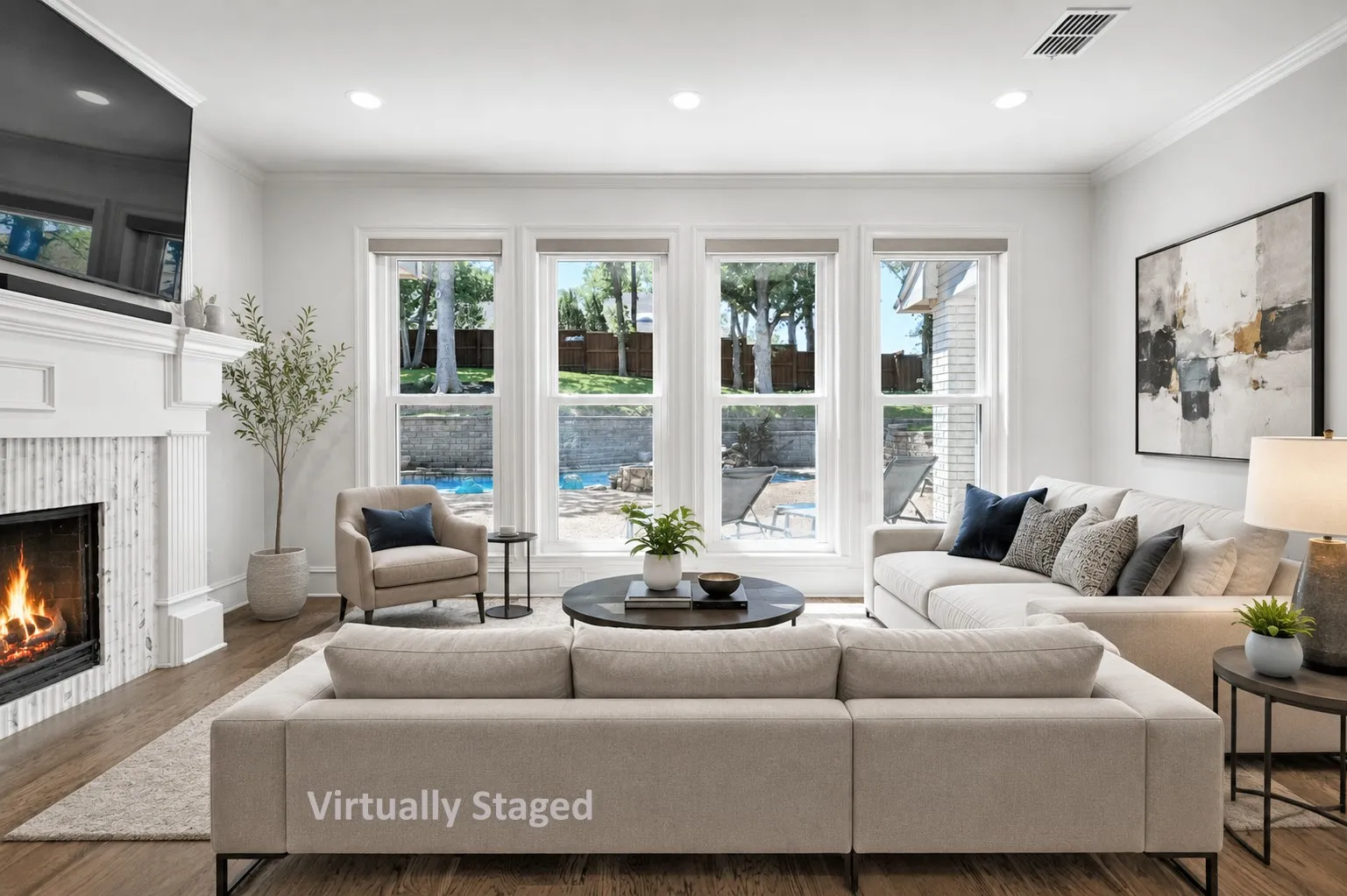 Virtually Staged: Bright living area featuring a fireplace with a white mantel and mosaic tile surround, recessed lighting, wood-finish flooring, and multiple large windows overlooking a backyard with a pool