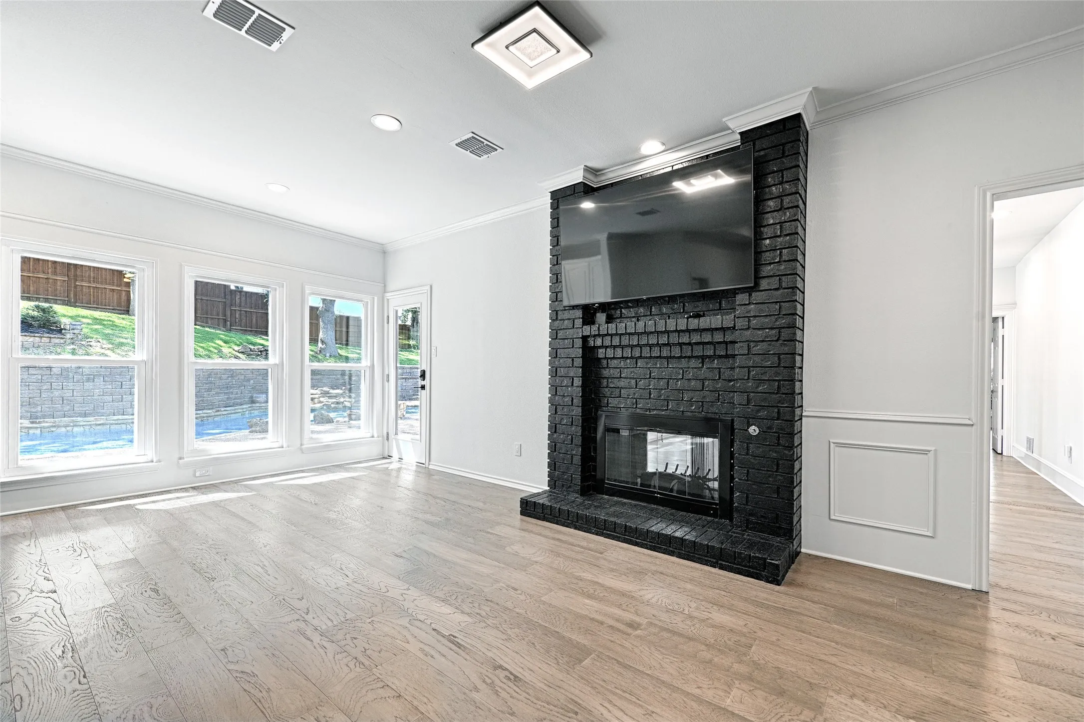 Living area featuring a black brick fireplace with a built-in firebox, wood-finish flooring, recessed lighting, and multiple windows