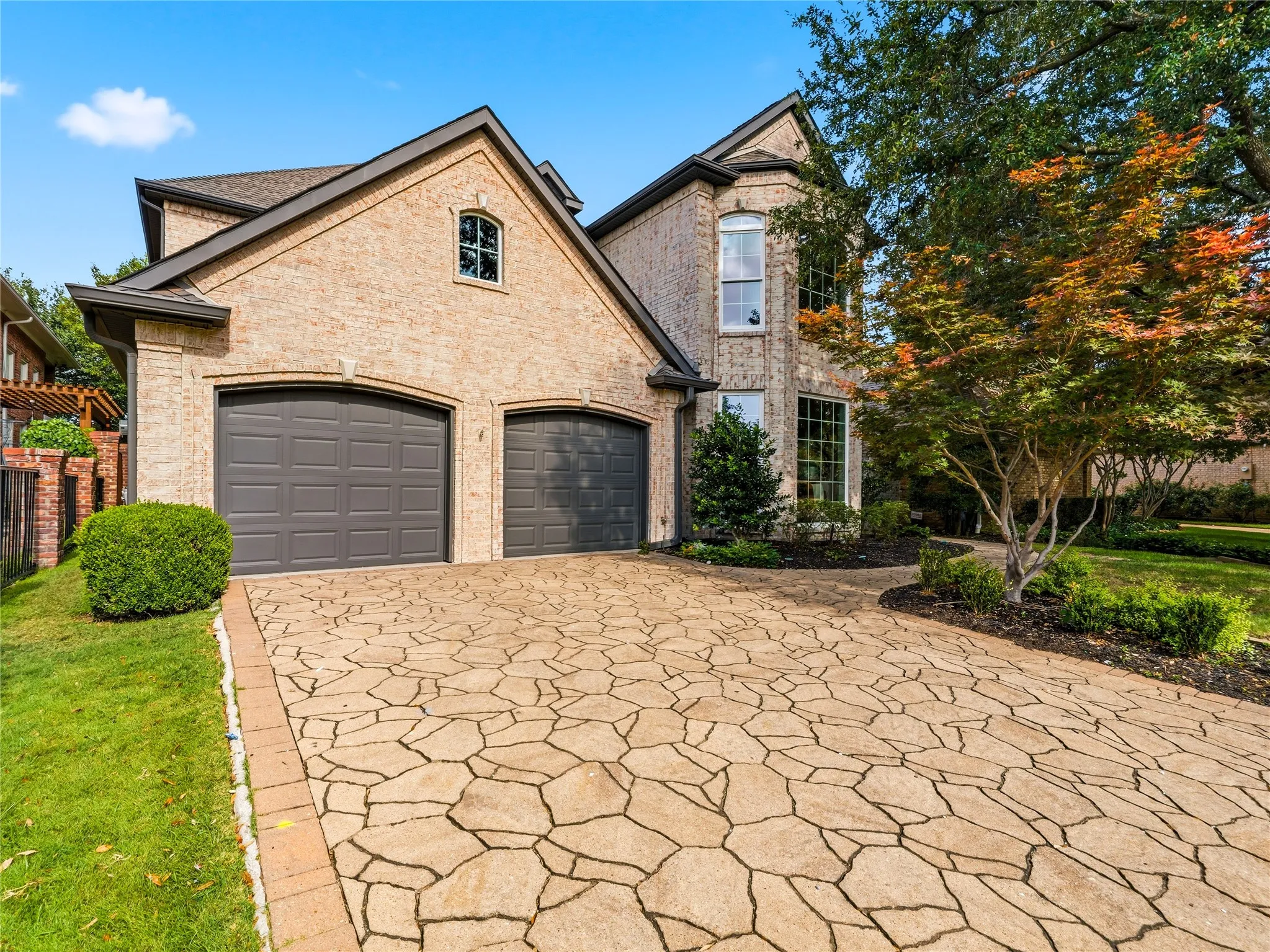 Brick exterior residence featuring a two-car garage with arched entrances, a patterned stone driveway, and mature landscaping