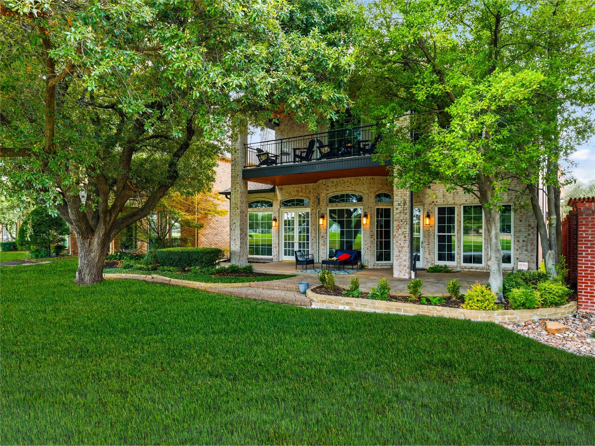 Rear exterior featuring a spacious patio, upper-level balcony, and extensive lawn