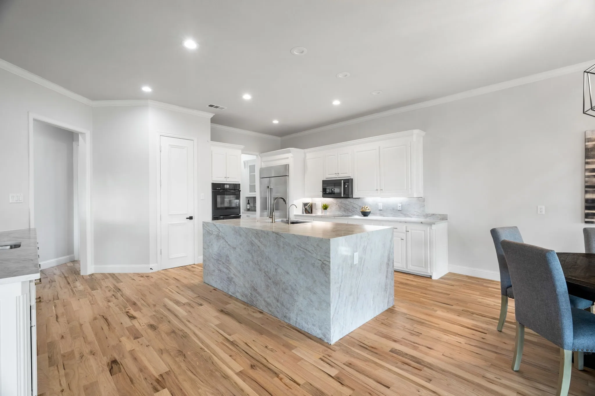 Kitchen featuring crown molding, light stone countertops, white cabinetry, recessed lighting, and an island with sink