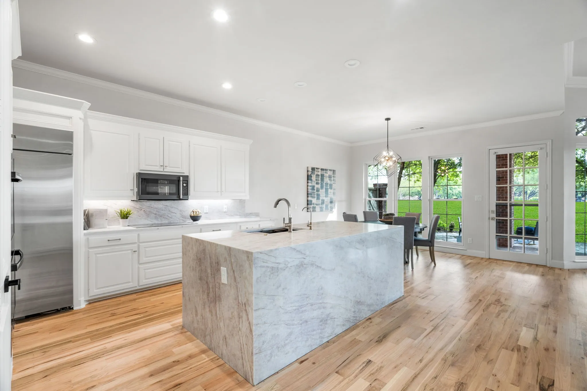 Kitchen with white cabinetry, stainless steel appliances, light stone countertops, light wood-type flooring, and ornamental molding