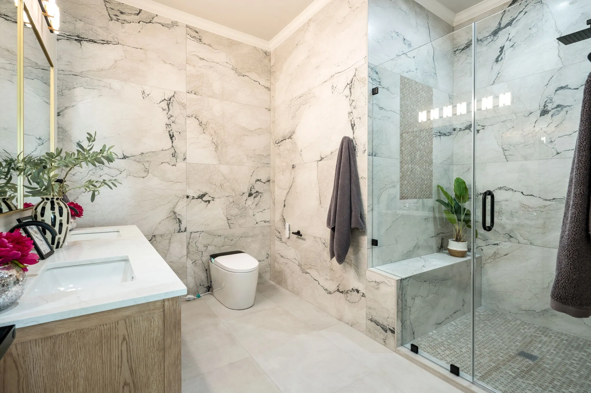 Full bathroom featuring double vanity, crown molding, a marble finish shower, and tile walls