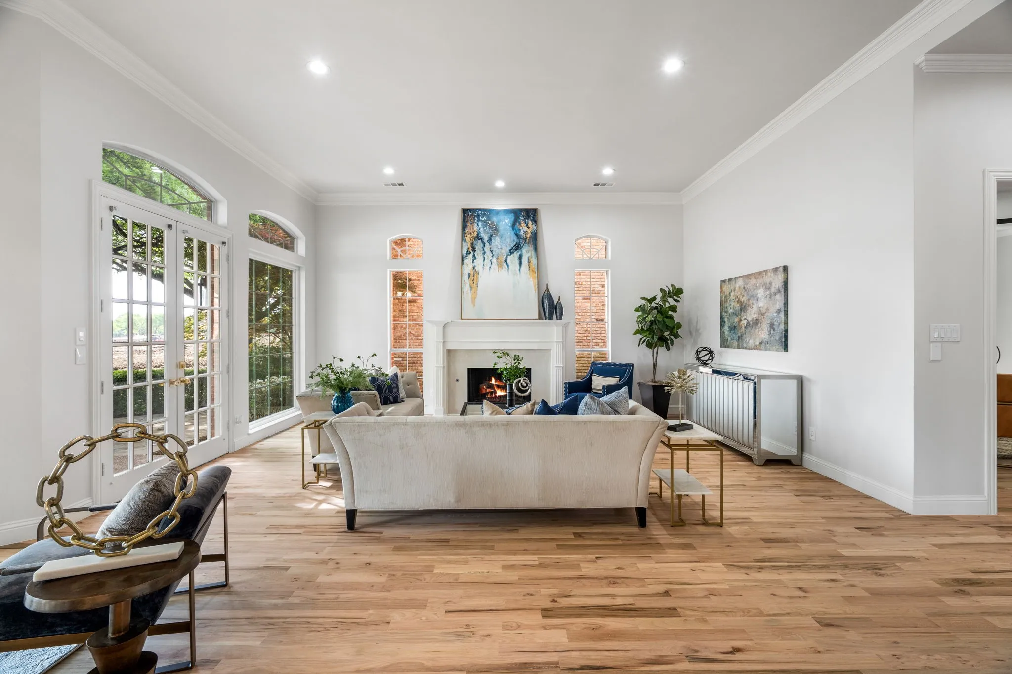 Living room featuring light wood-type flooring, recessed lighting, ornamental molding, a lit fireplace, and french doors