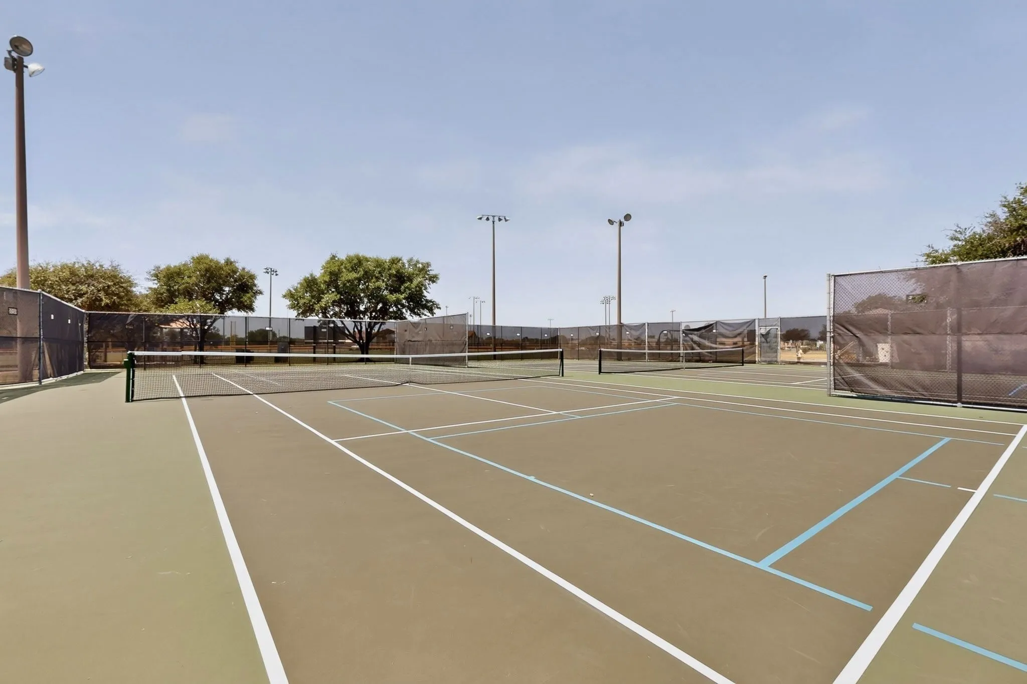Outdoor tennis courts featuring green and beige playing surfaces