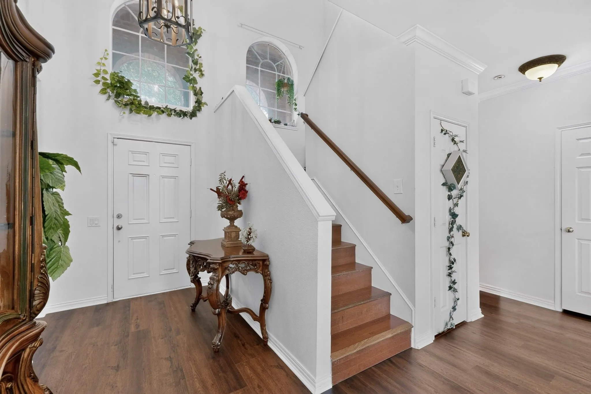 Foyer featuring wood-finish flooring, a grand staircase with wood treads and handrail, arched windows, and a panel-style entry door