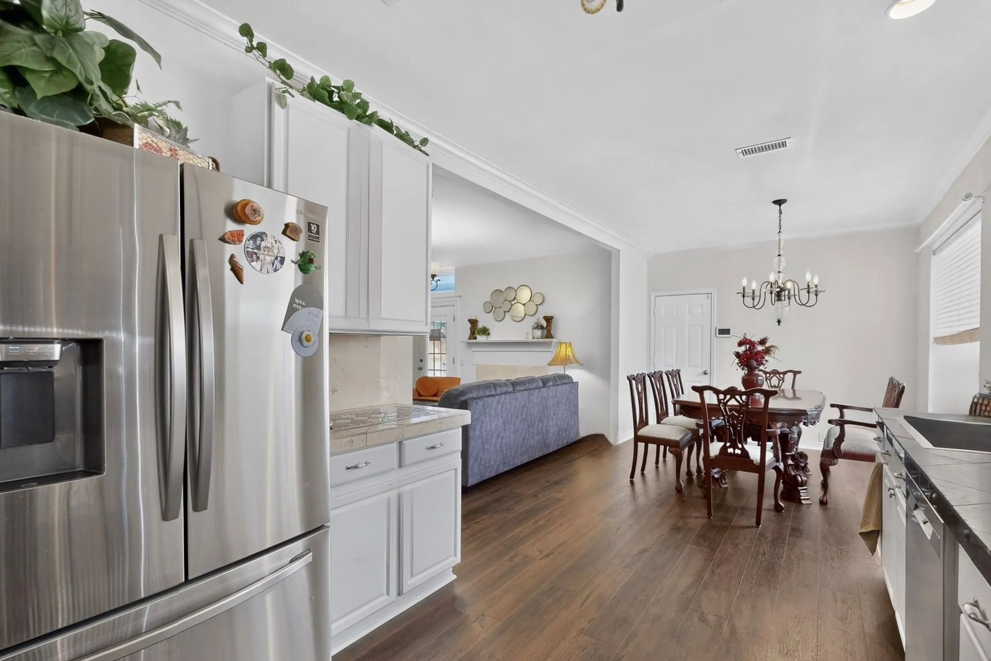 Open-concept living space featuring wood-finish flooring, white cabinetry, stainless steel refrigerator, and a recessed ceiling with crown molding