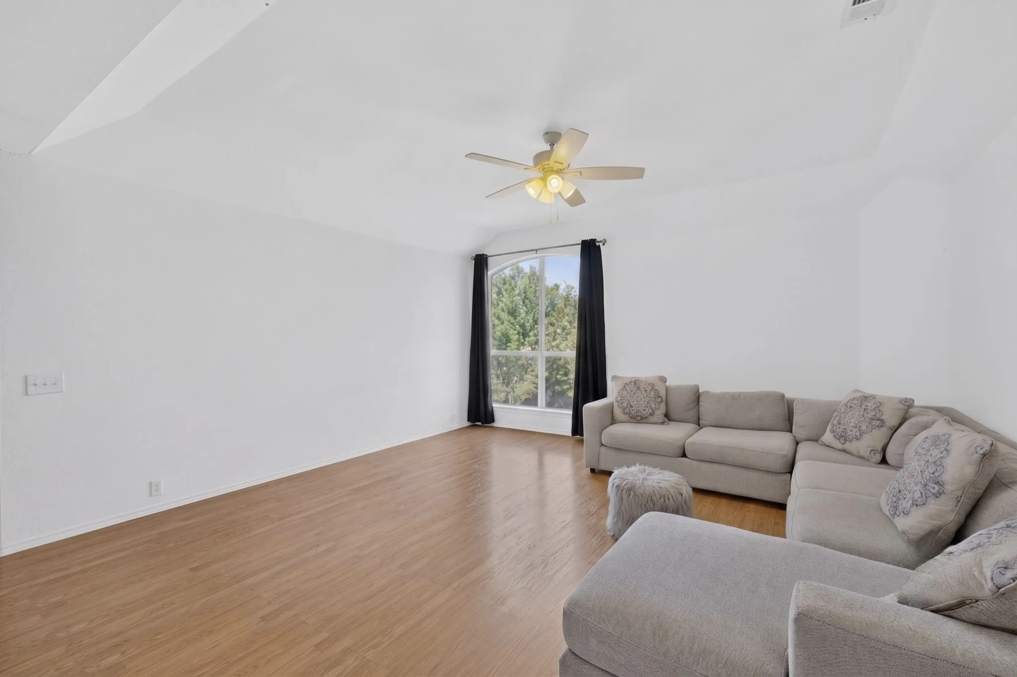 Spacious living area featuring wood-finish flooring, vaulted ceiling, and a ceiling fan with integrated lighting