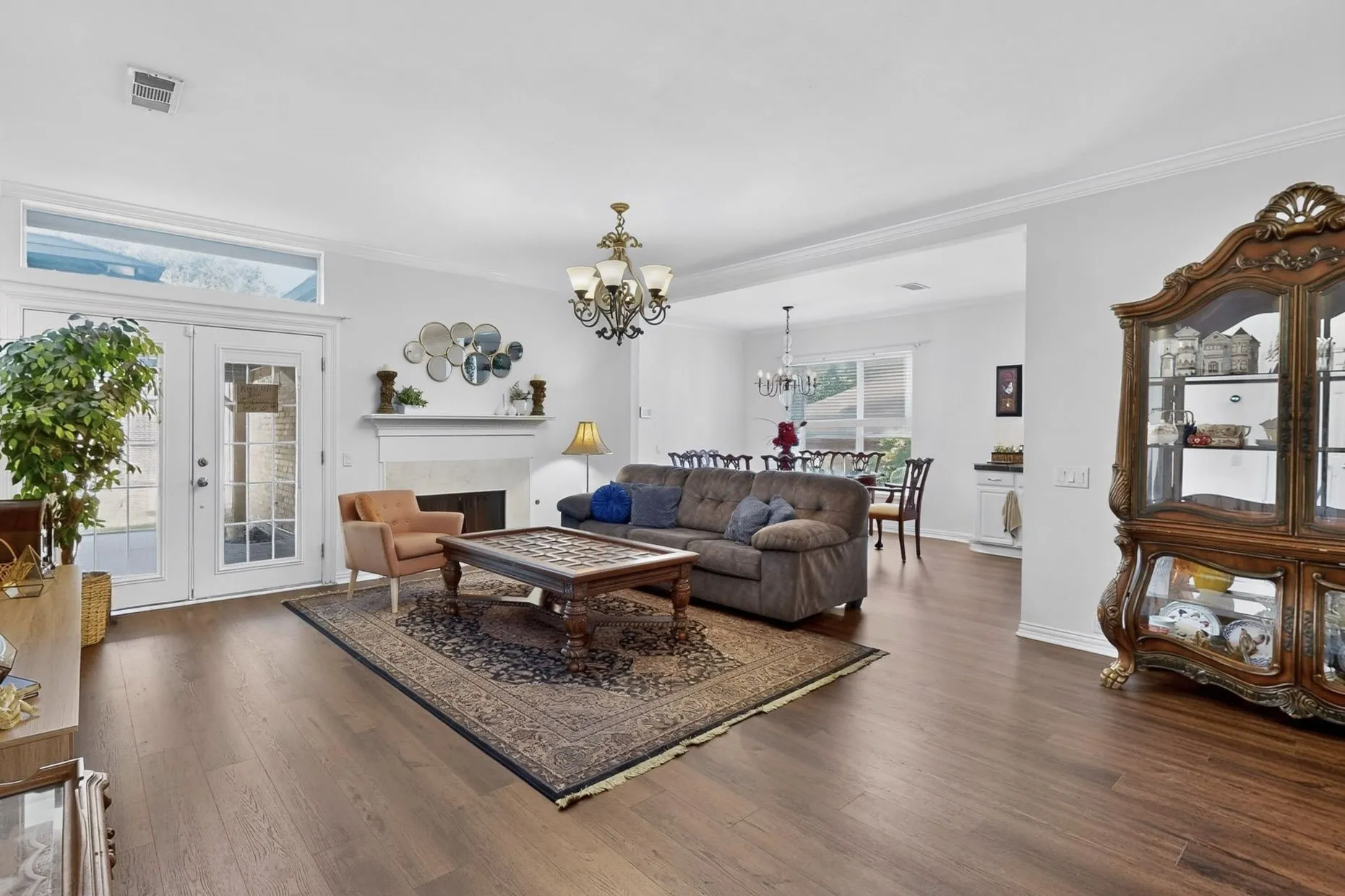 Living area with wood-finish flooring, a fireplace with mantel, and white double French doors with transom window