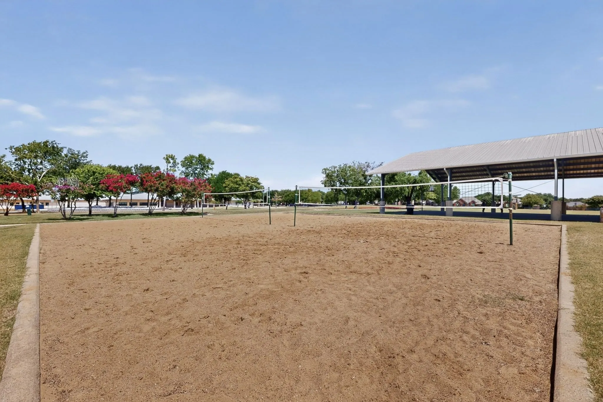 Sand volleyball court with multiple nets, framed by a concrete border