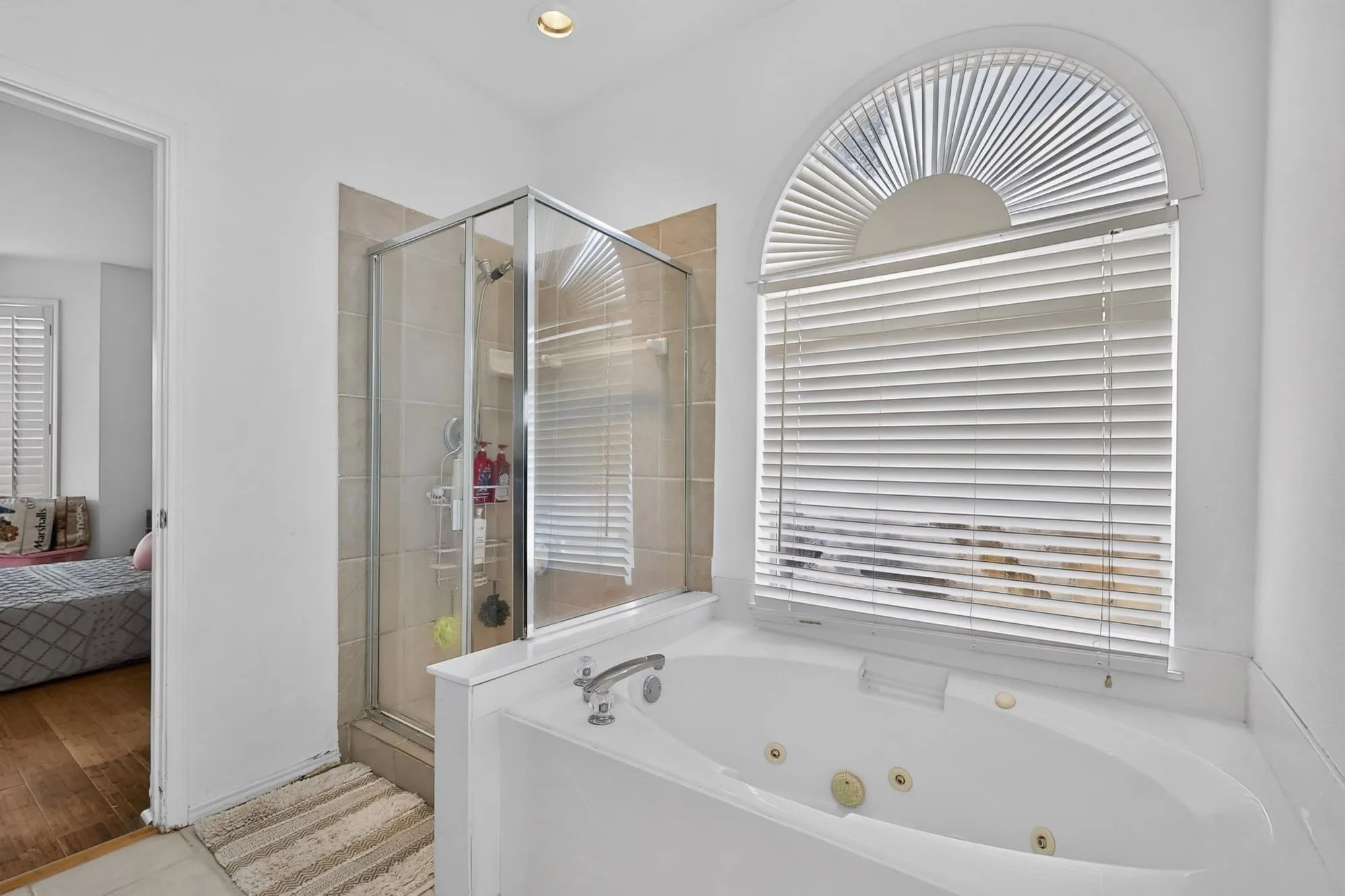 Bathroom featuring a built-in jetted tub, a separate glass-enclosed shower, and an arched window with blinds