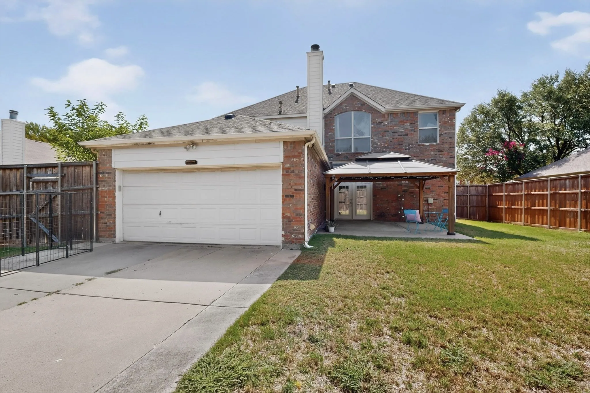 Brick exterior featuring a two-car garage, concrete driveway, and a fenced backyard with a patio