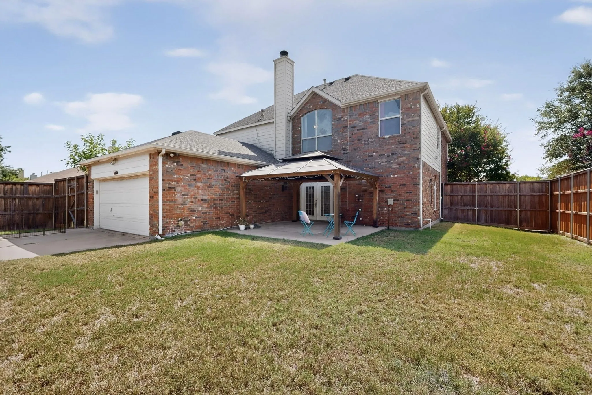 Brick and siding exterior featuring a covered patio with a gazebo structure, double glass doors, a two-car garage, and a fenced backyard