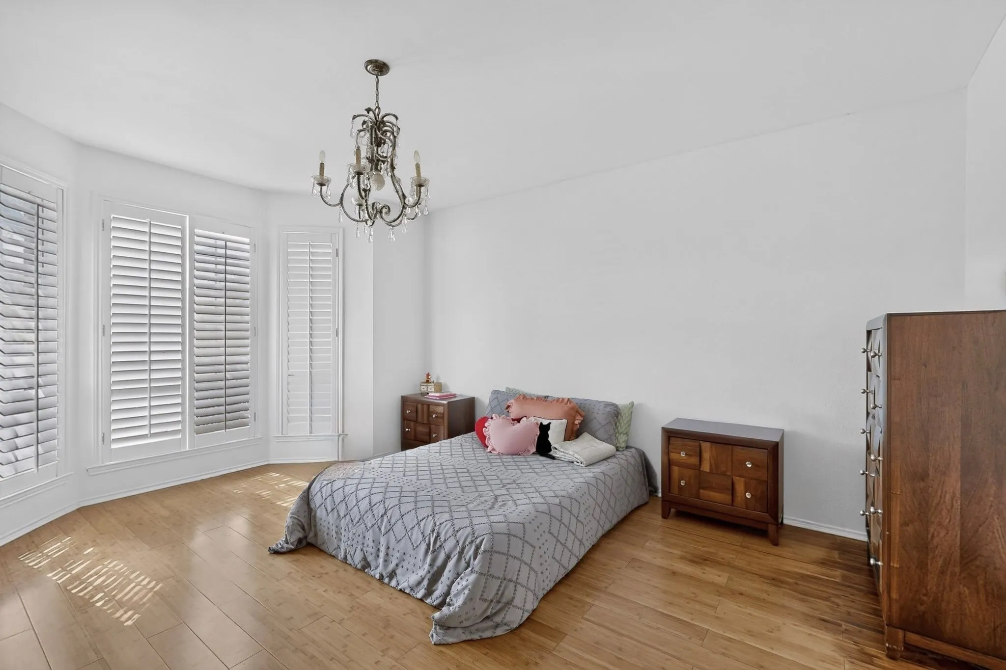 Bay window with white plantation shutters, wood-finish flooring, and a decorative chandelier