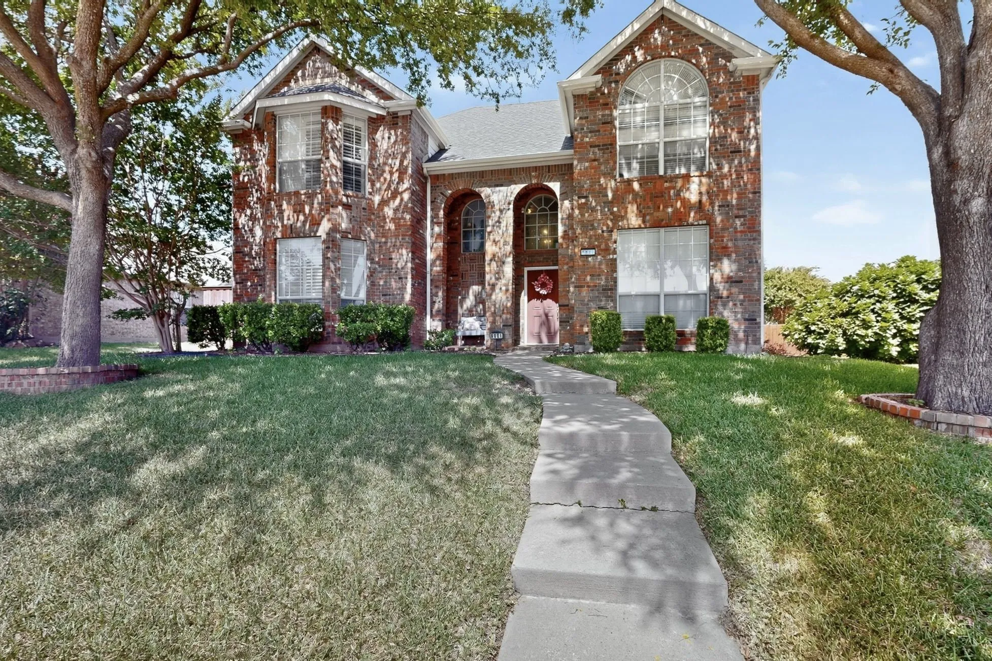 Traditional brick-front home with a gabled roofline, arched entry, bay window, and mature trees