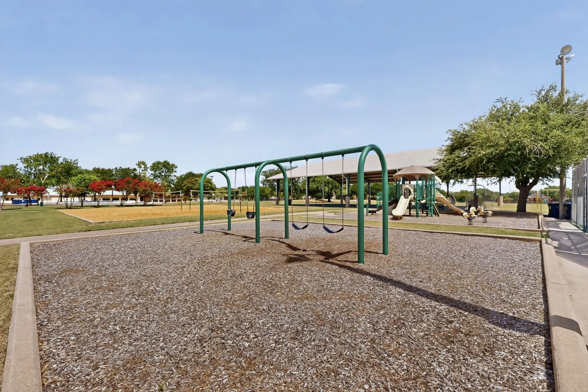 Community playground featuring a swing set, covered play structures, and mature shade trees