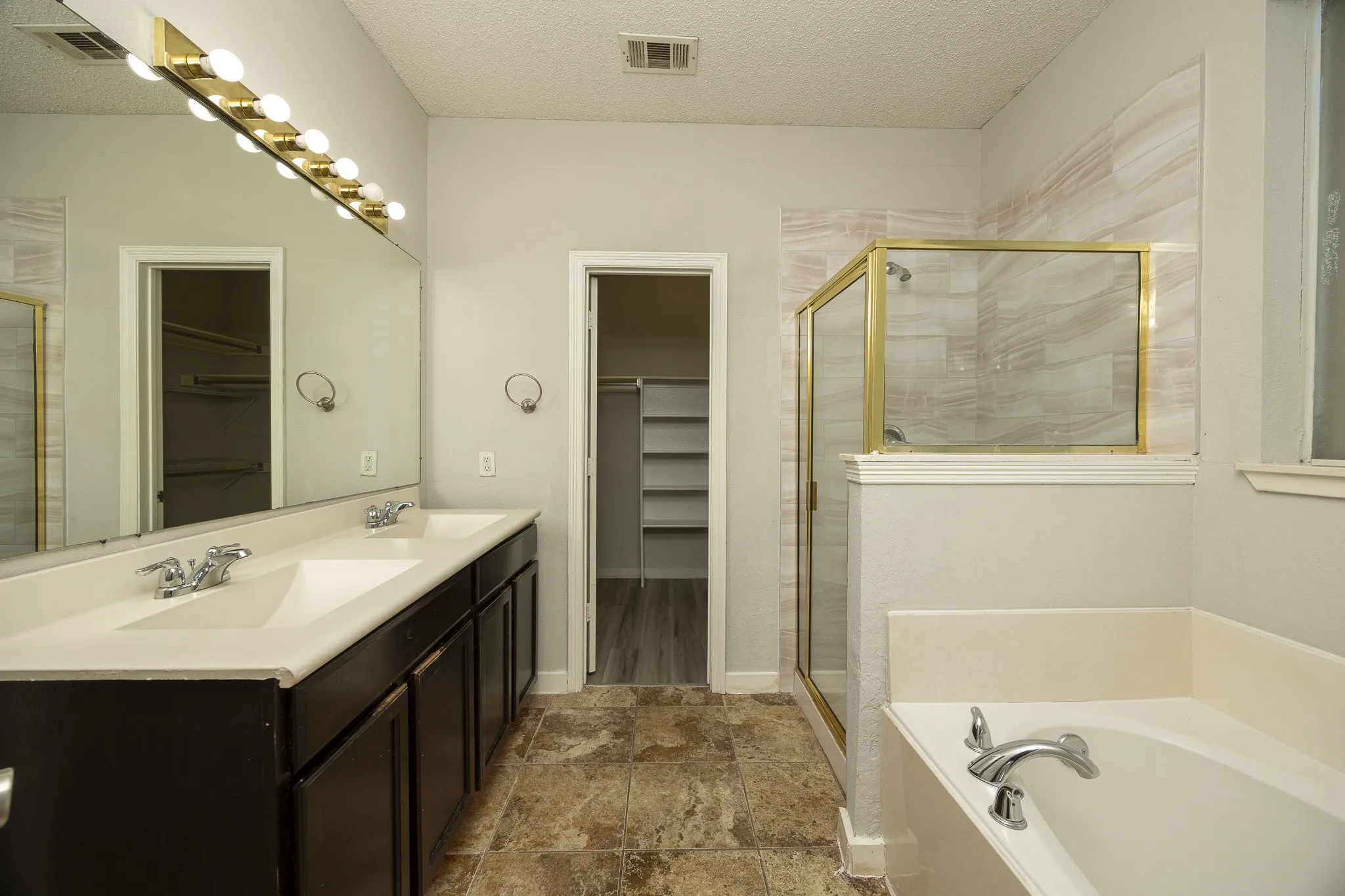 Dual vanity with integrated sinks, a built-in soaking tub, a stand-alone shower with a glass enclosure, and wood-finish flooring