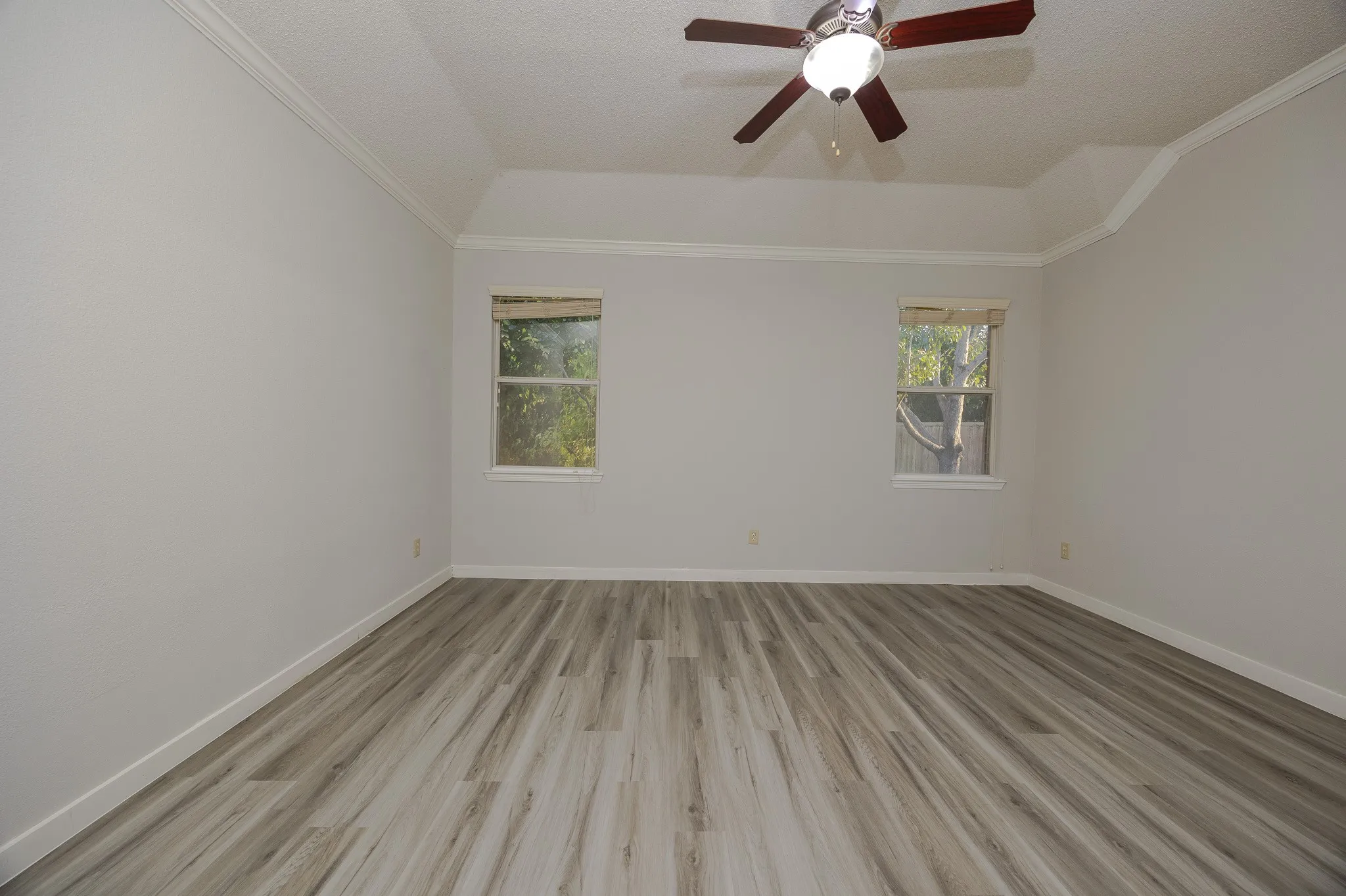 Recessed ceiling with an attached ceiling fan, crown molding, two windows with blinds, and wood-finish flooring